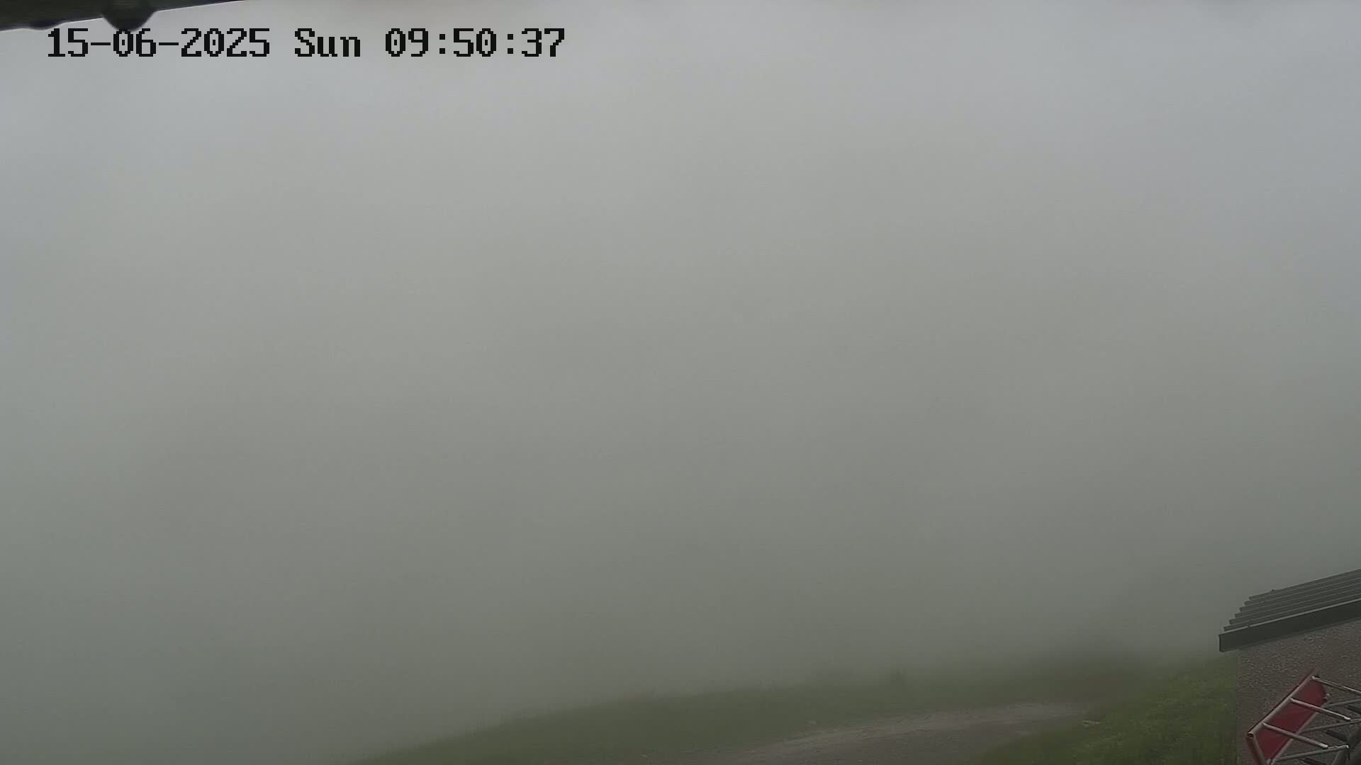 A thick fog obscures the view of a grassy area and part of a building.