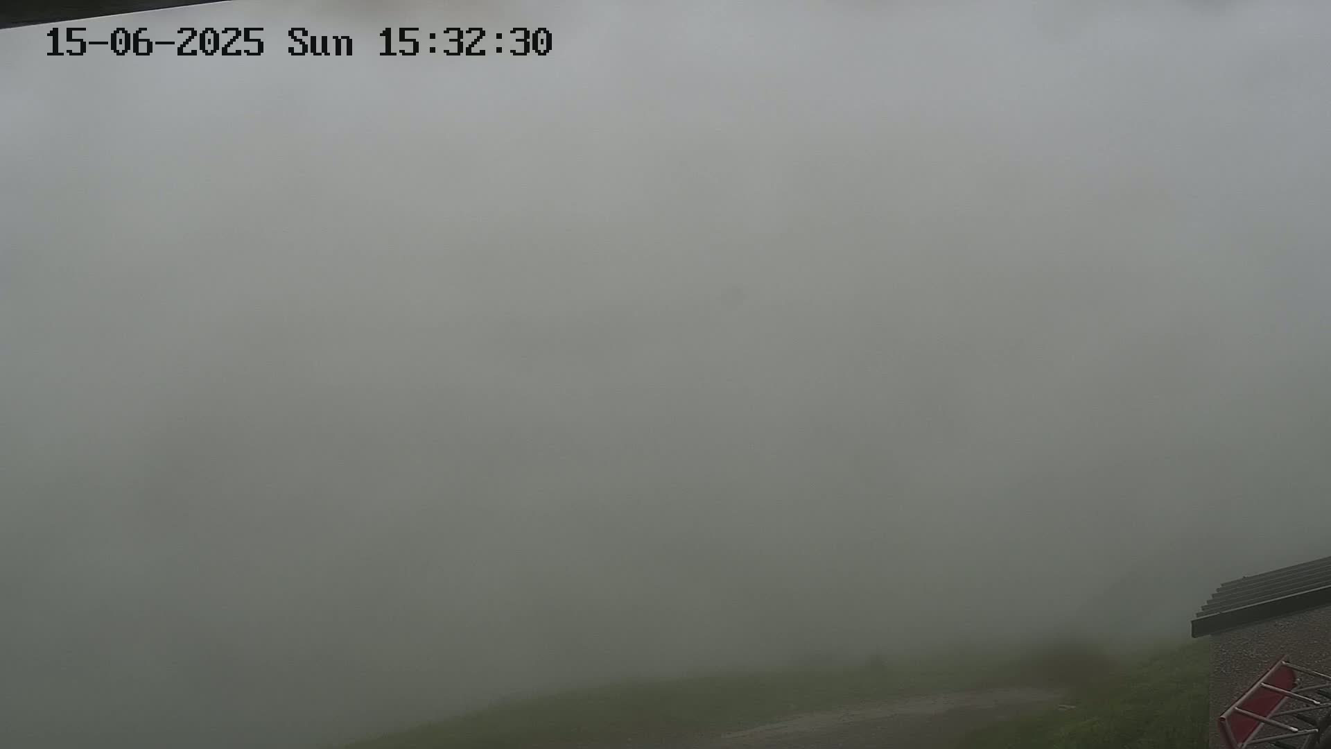 A thick fog obscures the view of a grassy area and a portion of a building in the bottom right corner.
