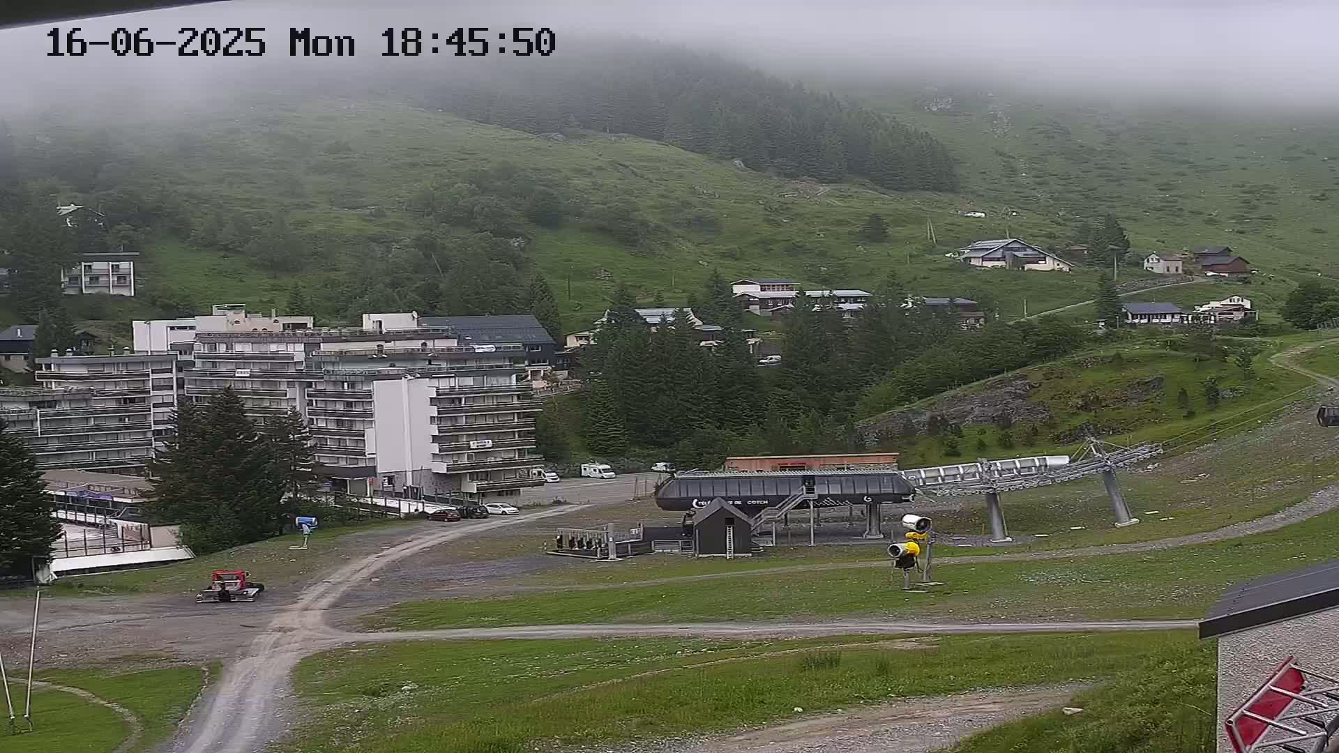 A foggy mountainside view shows a ski lift, several buildings, and a parking lot.