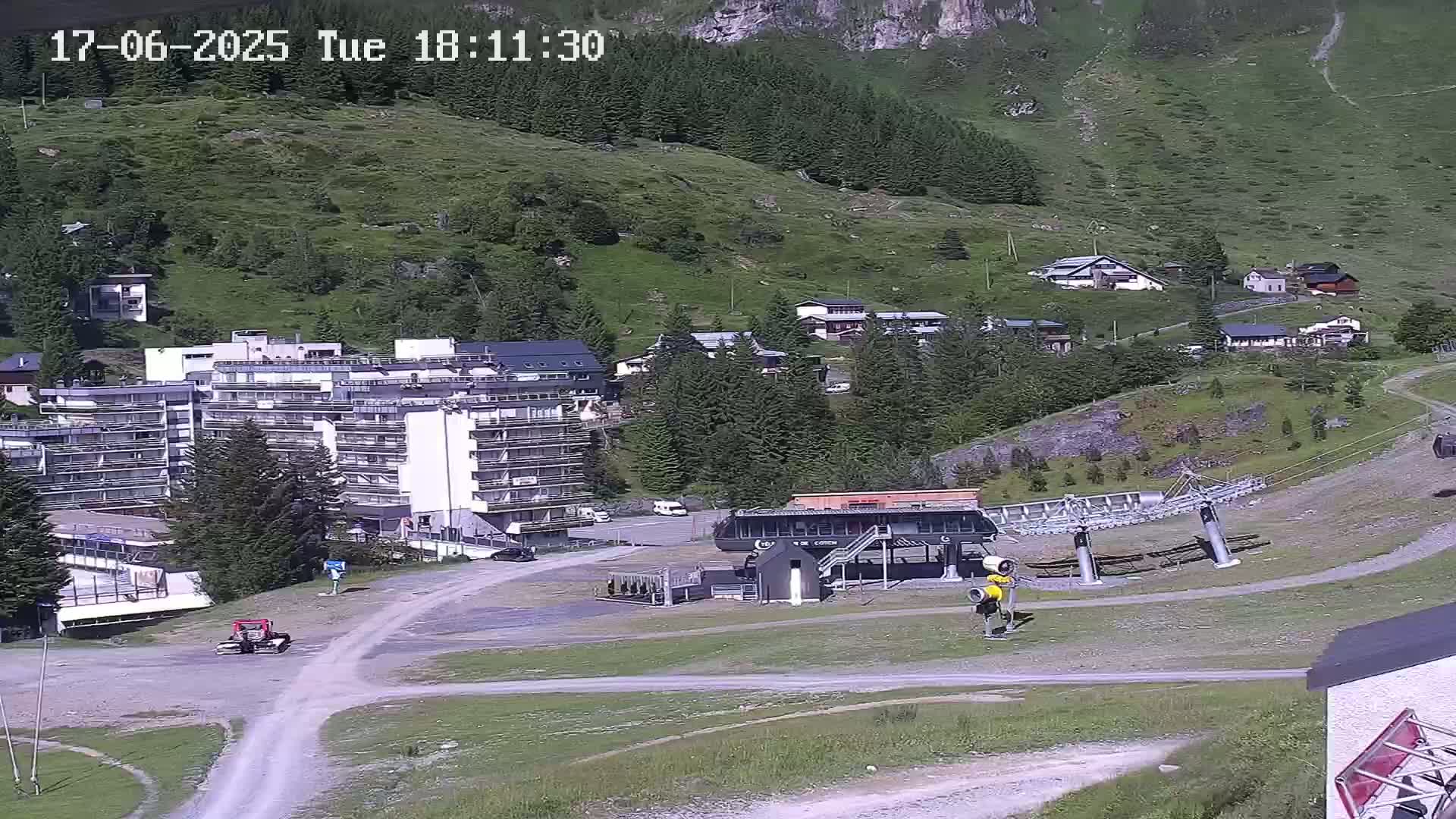 A ski lift base station and several buildings are situated on a hillside, with a partly sunny sky.