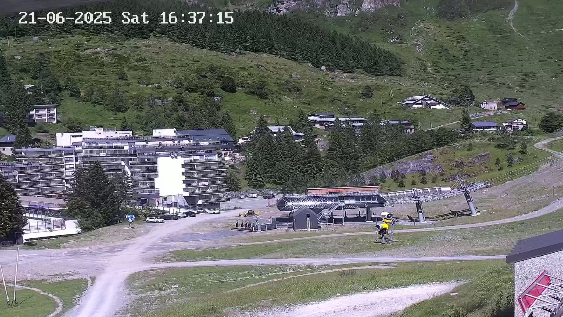 A ski lift base station and several buildings are situated in a mountainous area on a sunny day.