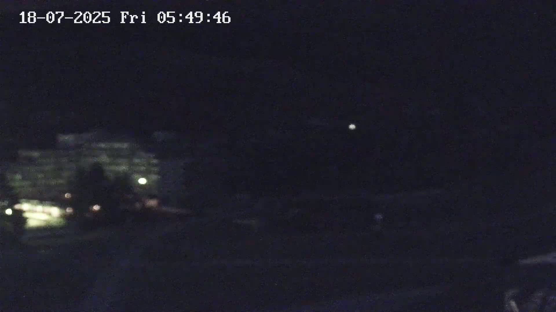A blurry, nighttime image shows a dimly lit building and a bright light in the dark sky.