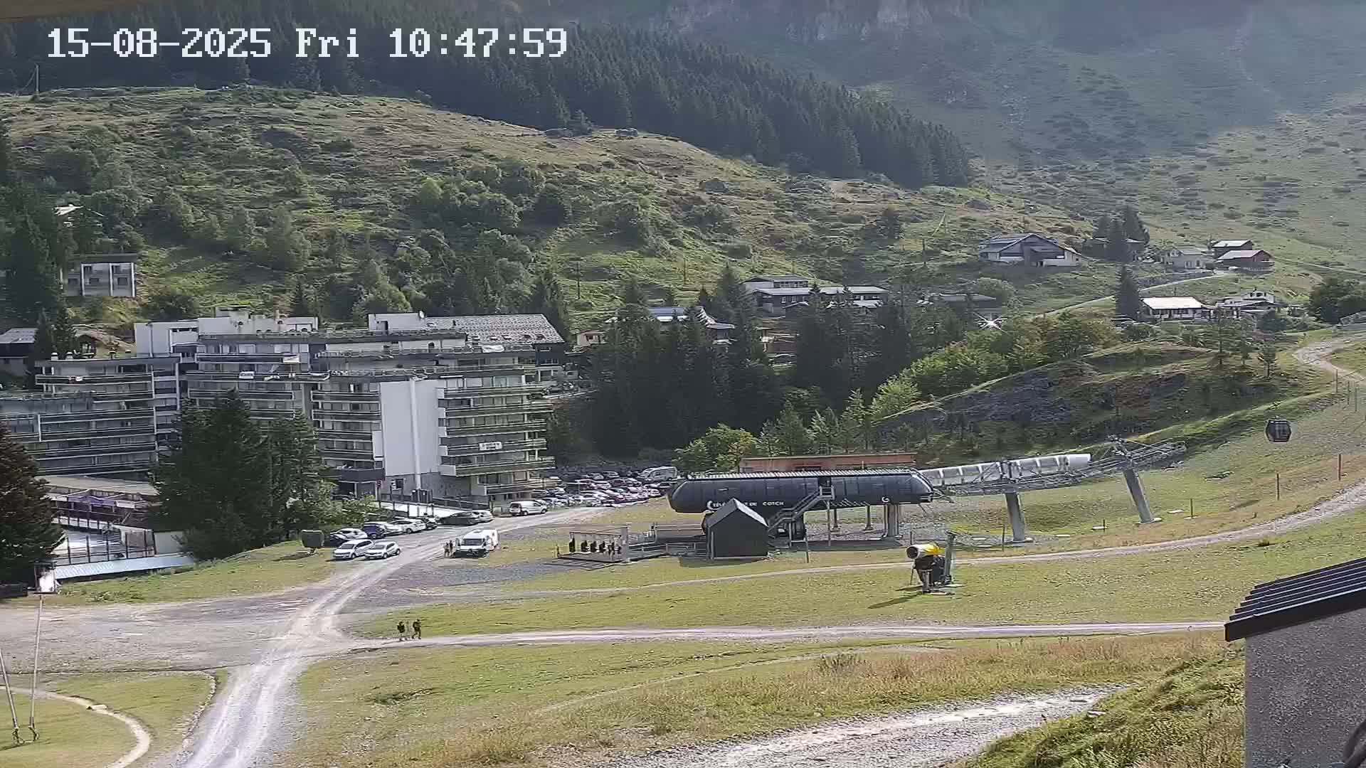 A mountainside village scene at dusk shows a multi-story building, smaller houses, a chairlift, and a parking lot.
