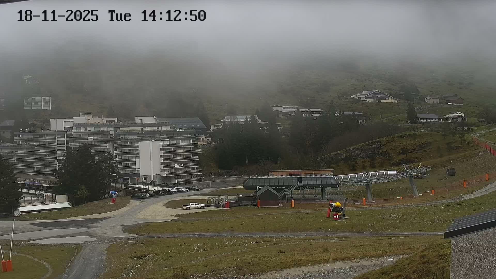 A mountainside village scene at dusk shows a multi-story building, smaller houses, a chairlift, and a parking lot.