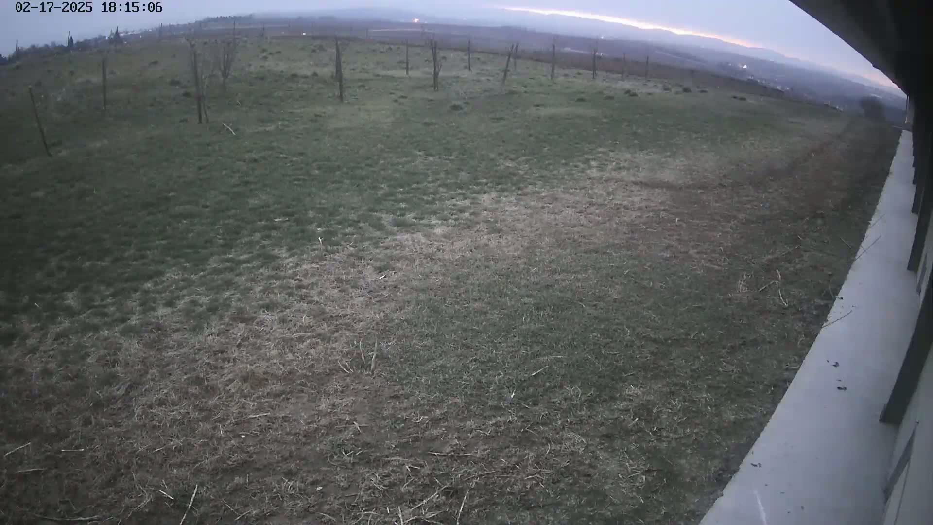 A view from a high angle shows a patchy lawn leading to a distant, hazy landscape under a twilight sky.