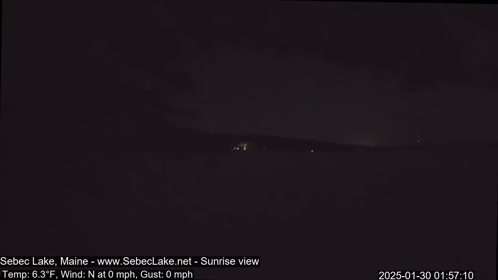 A dark, nighttime landscape is visible with a few faint lights in the distance under a mostly cloudy sky.