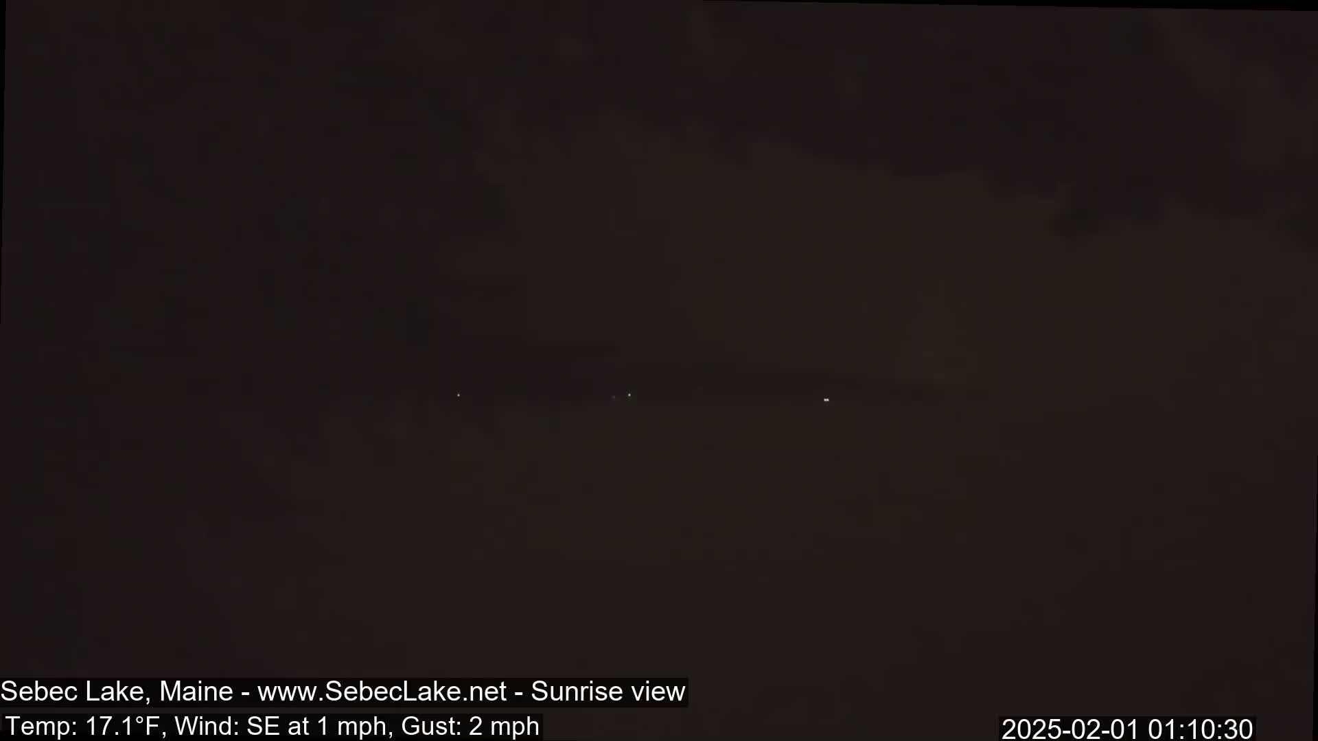 A dark, nighttime scene shows a few distant lights on a hazy horizon under a cloudy sky, with a southeast wind at 1 mph and gusts up to 2 mph and a temperature of 17.1°F.