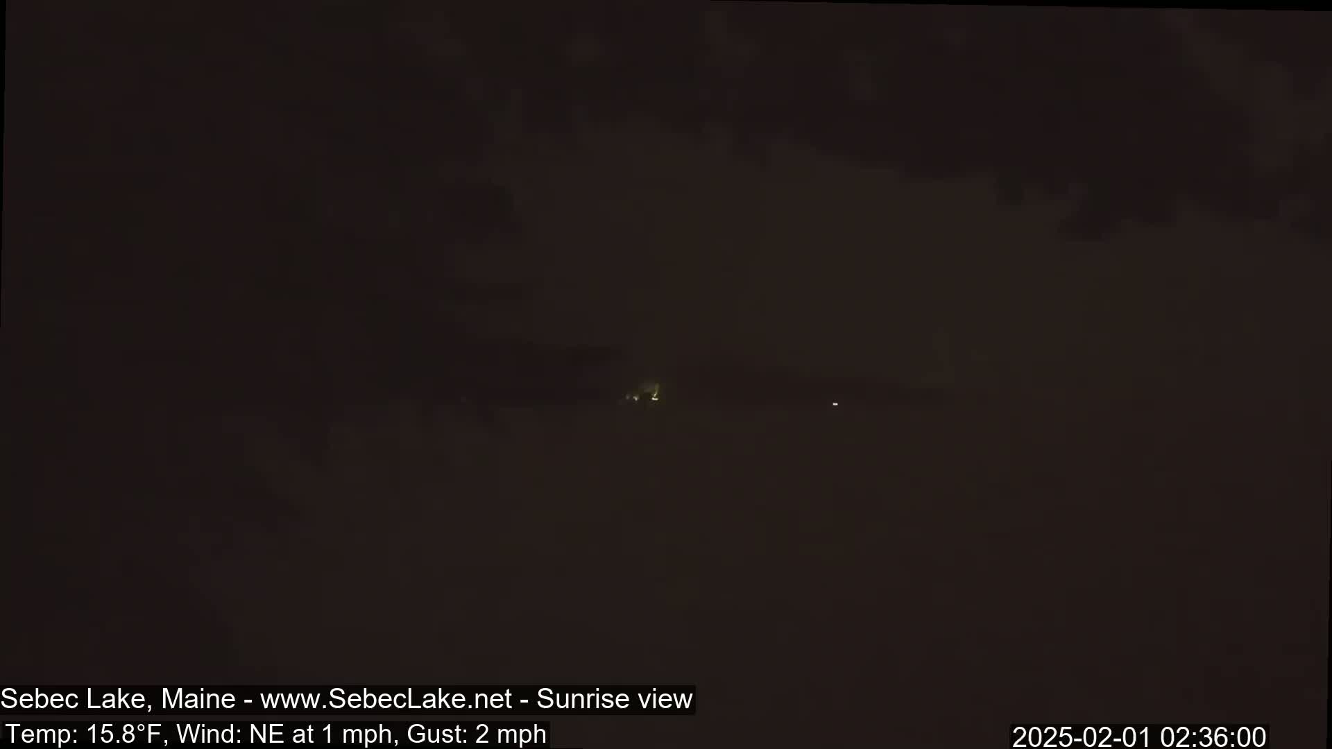 A dark, nighttime landscape is visible, with a few faint lights in the distance under a cloudy sky.