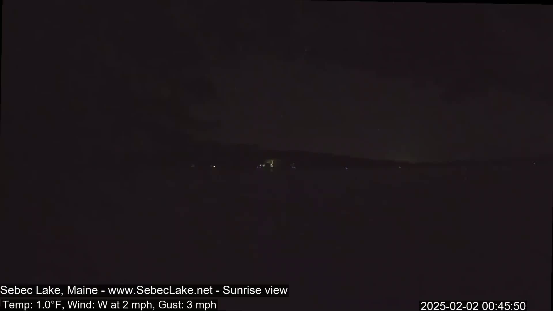 A dark, nighttime view of a lake with a distant, faintly lit shoreline under a cloudy sky, with a temperature of 1°F and a westerly wind.