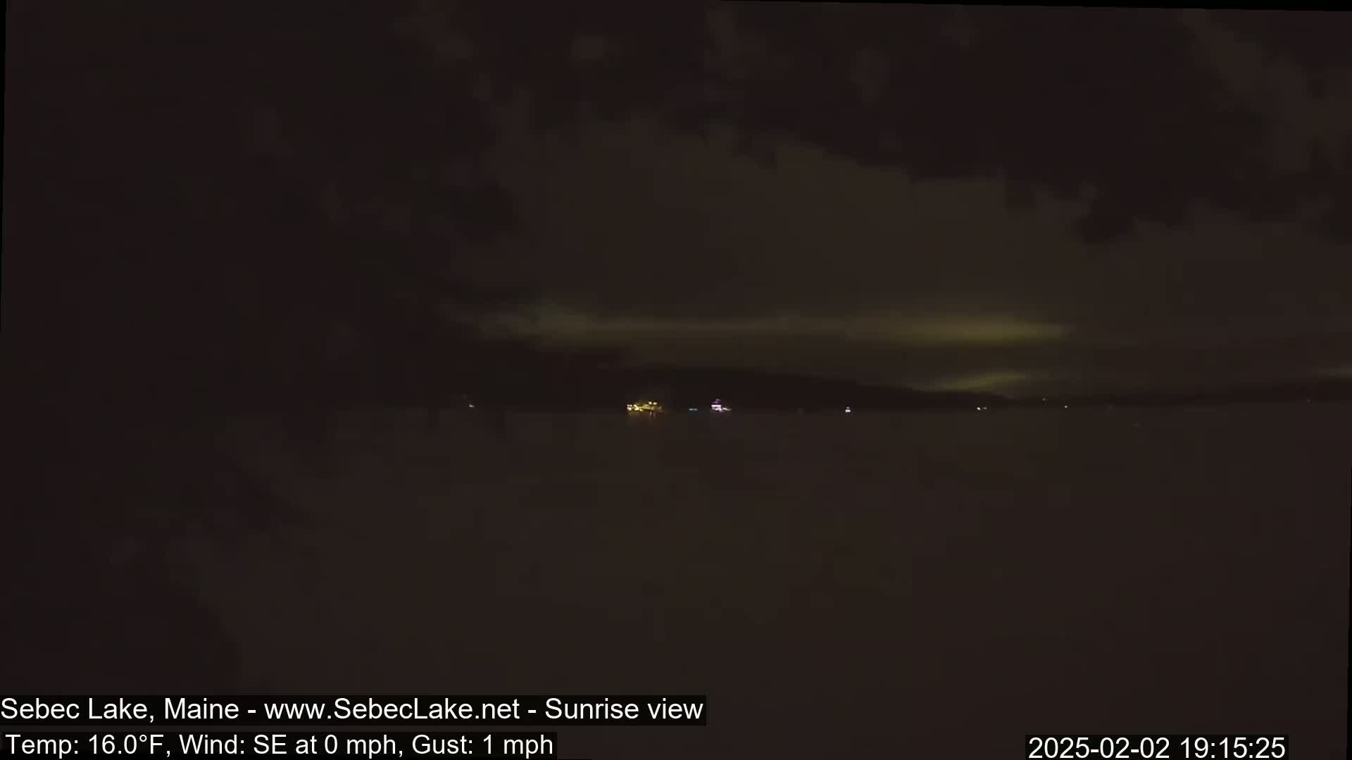 A nighttime view of a dark lake with a few distant lights and a cloudy sky.