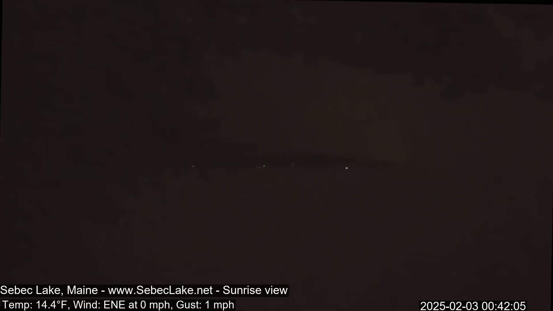 A dark, foggy, nighttime scene shows a few faint lights in the distance under a mostly cloudy sky.