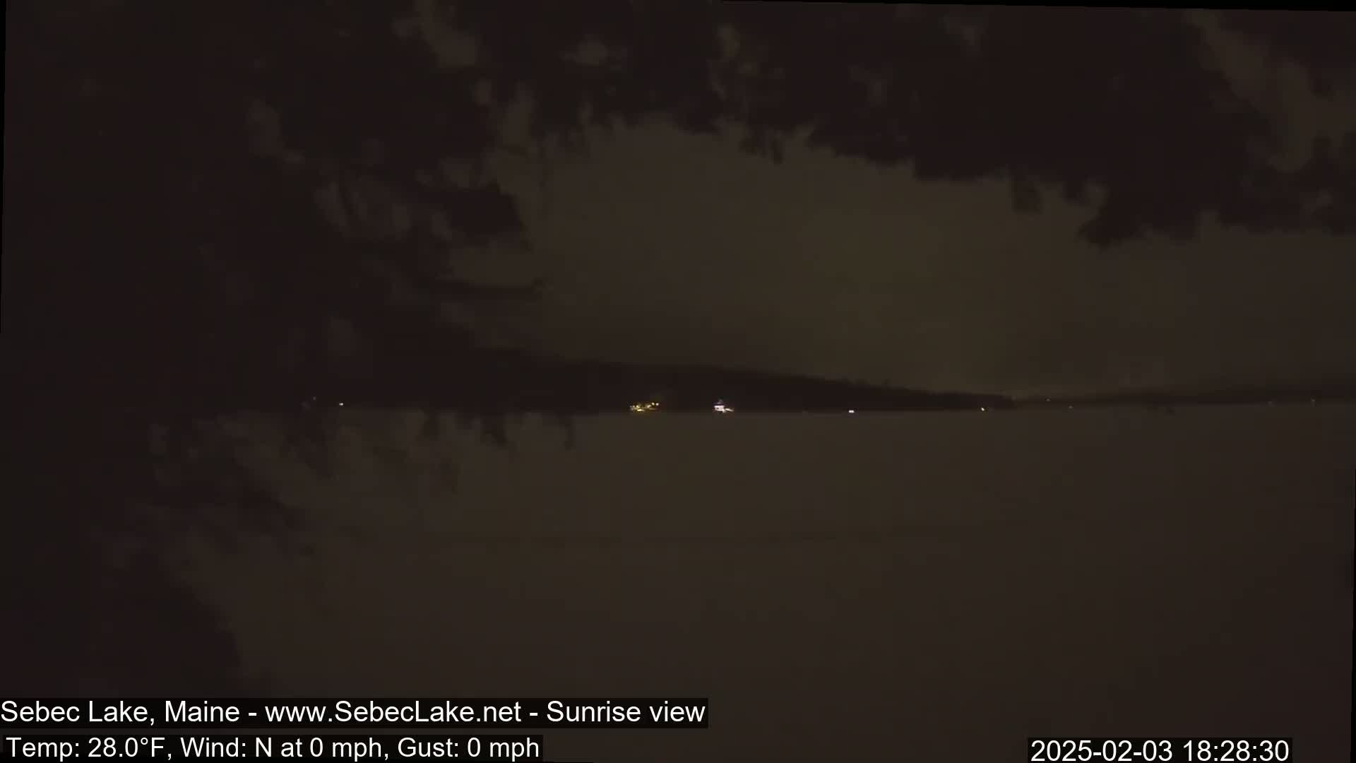 A dark, nighttime view of a calm lake under a cloudy sky.
