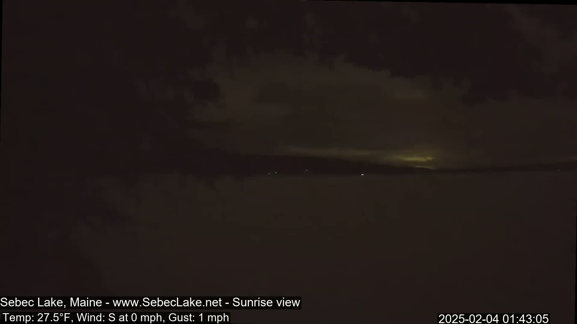 A dark, nighttime view of a lake under a cloudy sky.