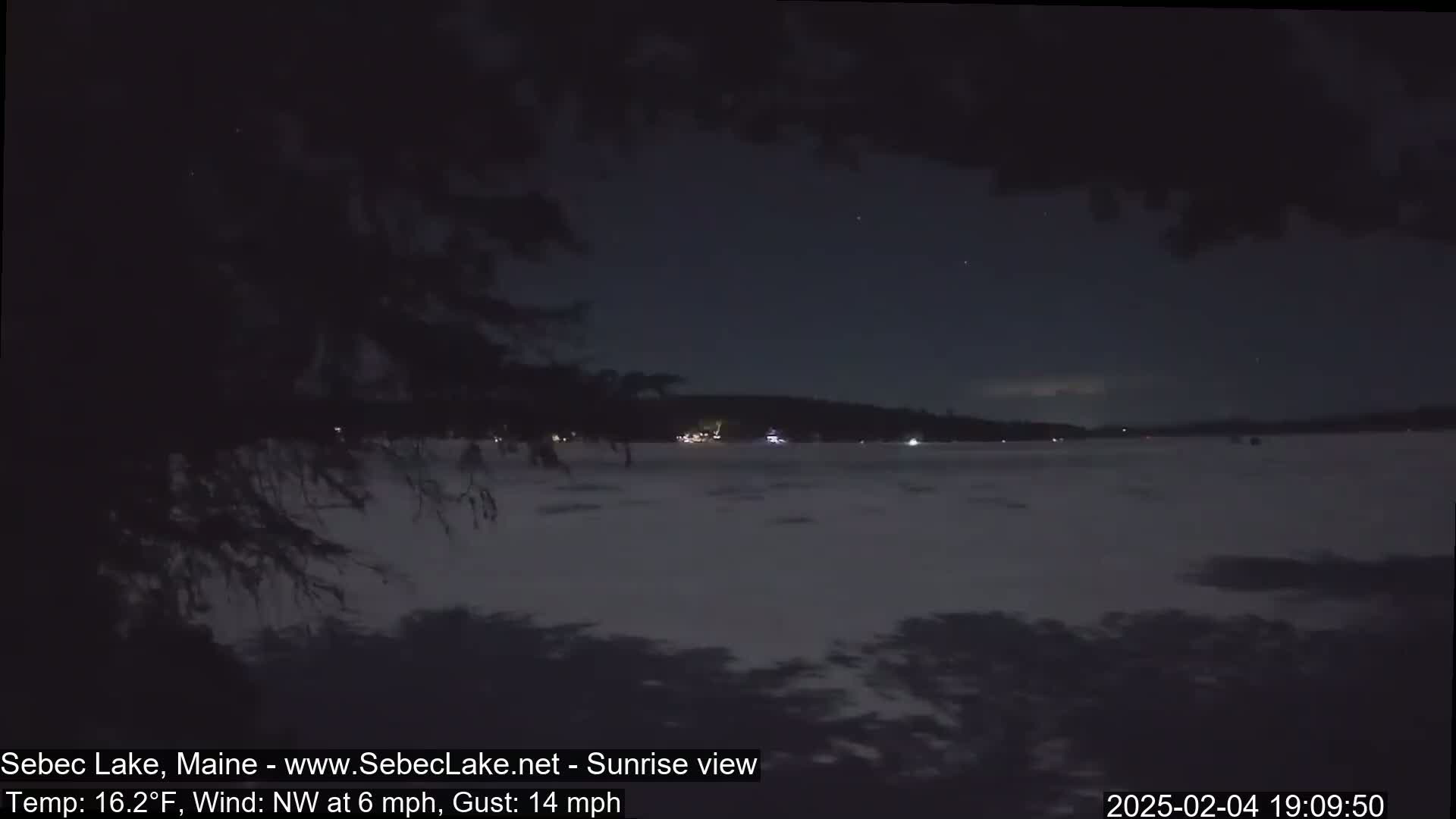 A nighttime view of a snow-covered lake under a dark sky with a few stars visible, and a slight wind.