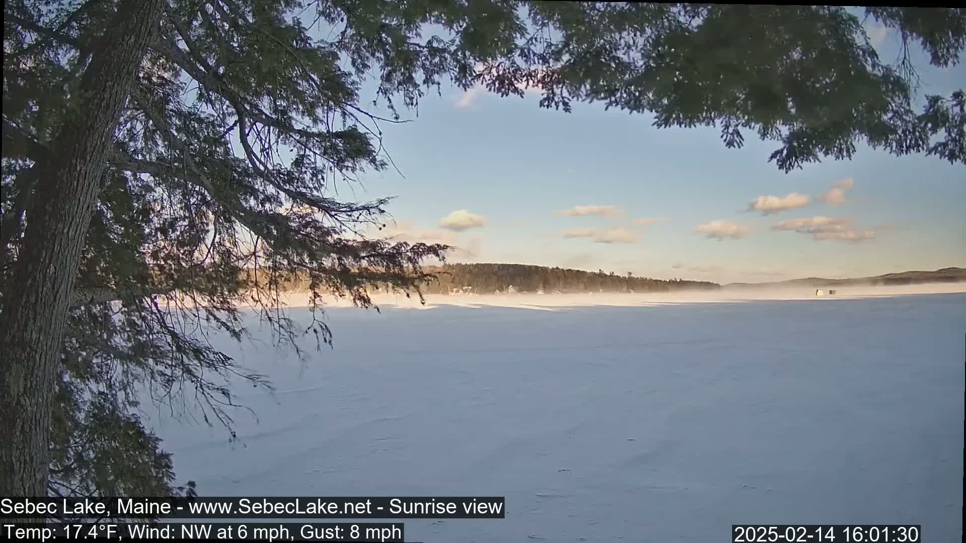 A partially obscured view of a snow-covered lake under a partly cloudy sky with a light wind.
