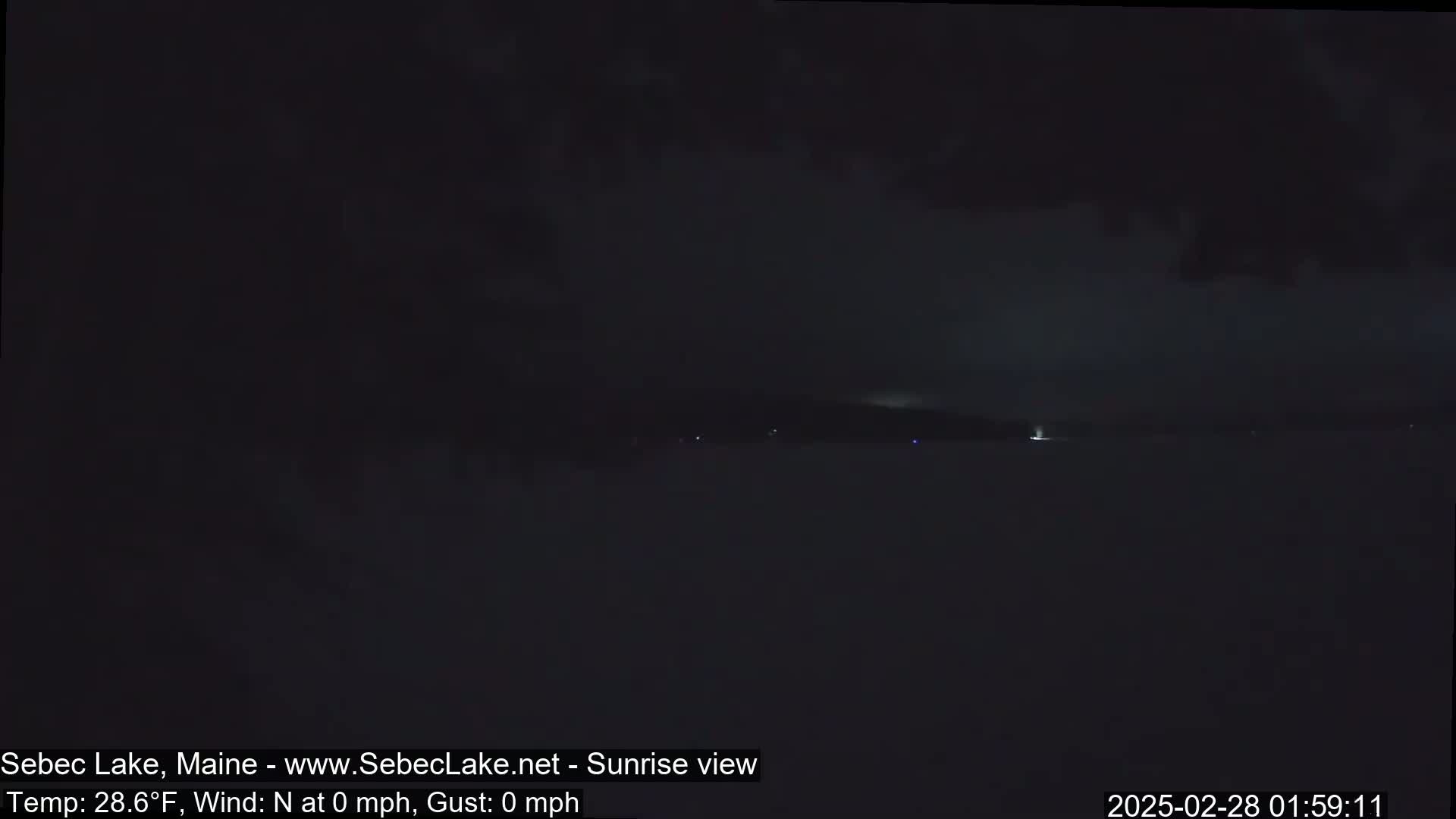 A dark, nighttime view of a calm body of water under a mostly cloudy sky.