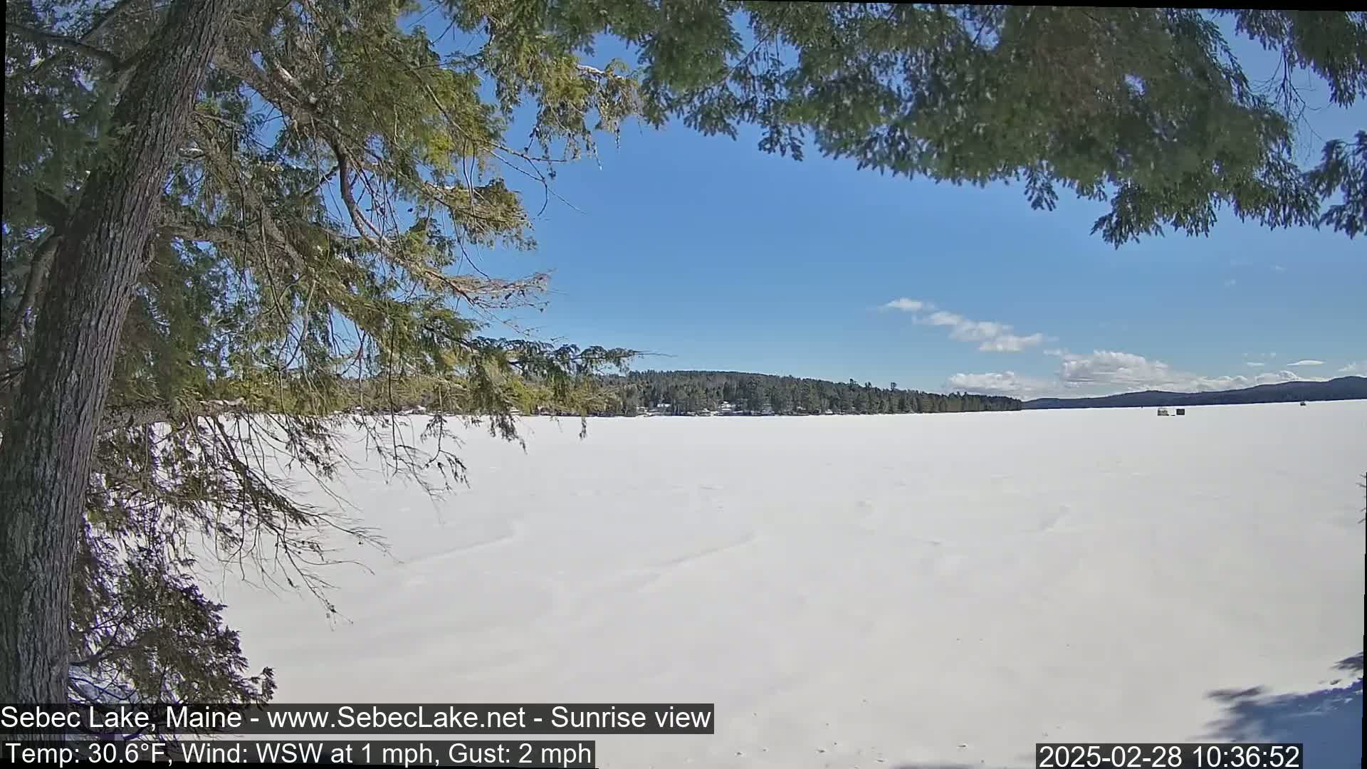 A snow-covered frozen lake stretches to a distant treeline under a mostly clear blue sky.