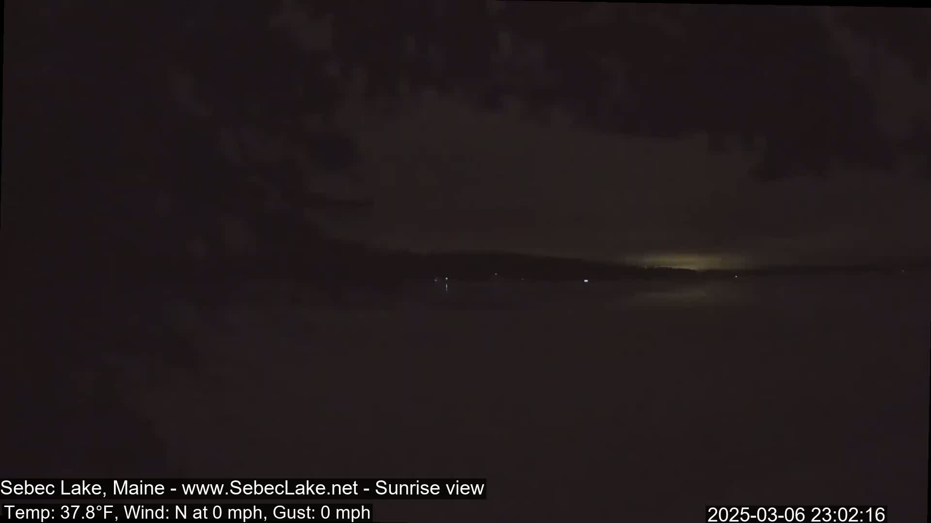 A dark, nighttime view of a calm lake with a faint, illuminated horizon.