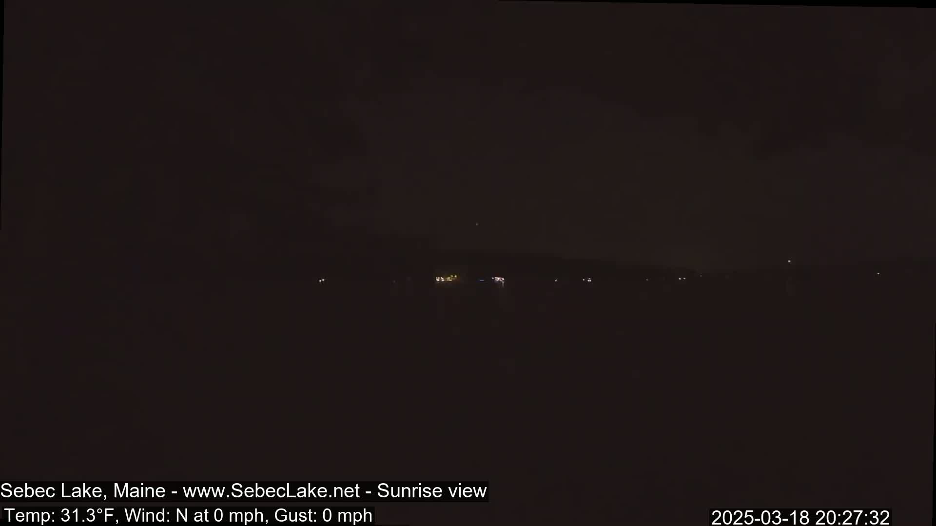 A dark, nighttime landscape is visible, showing a few faint lights in the distance under a mostly clear sky.