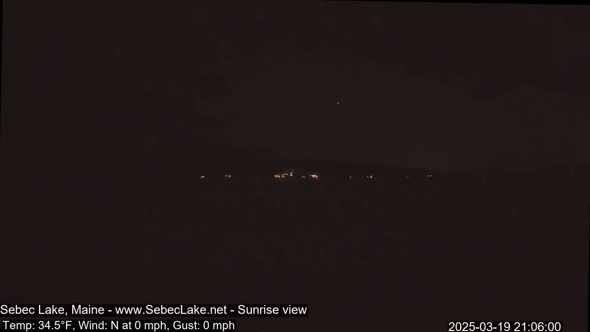 A dark, nighttime scene shows a distant line of faint lights across a dark horizon under a clear, dark sky.