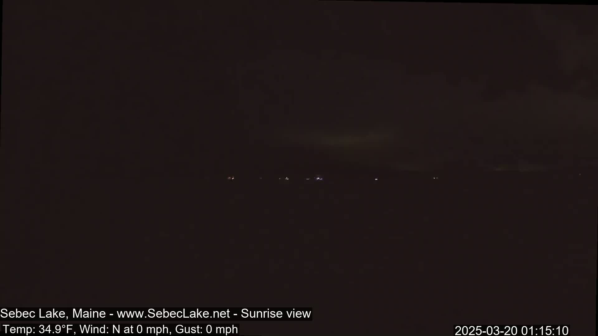 A dark, nighttime landscape shows a few distant lights on the horizon under a mostly clear sky.