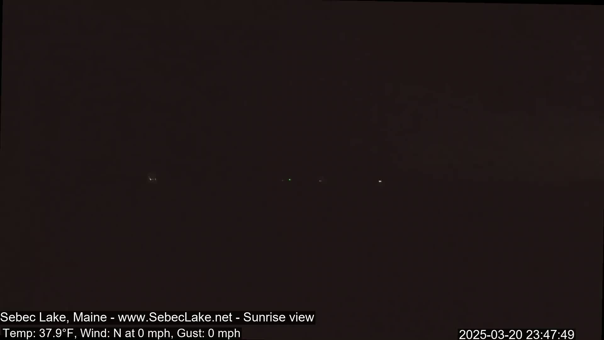 A dark, nighttime scene with a few distant lights visible under a calm, clear sky.