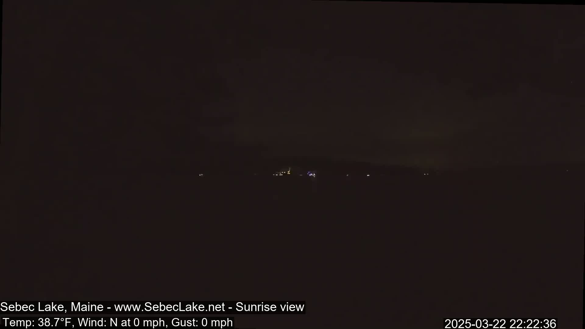 A dark, nighttime view of a distant, dimly lit landscape under a mostly clear sky.