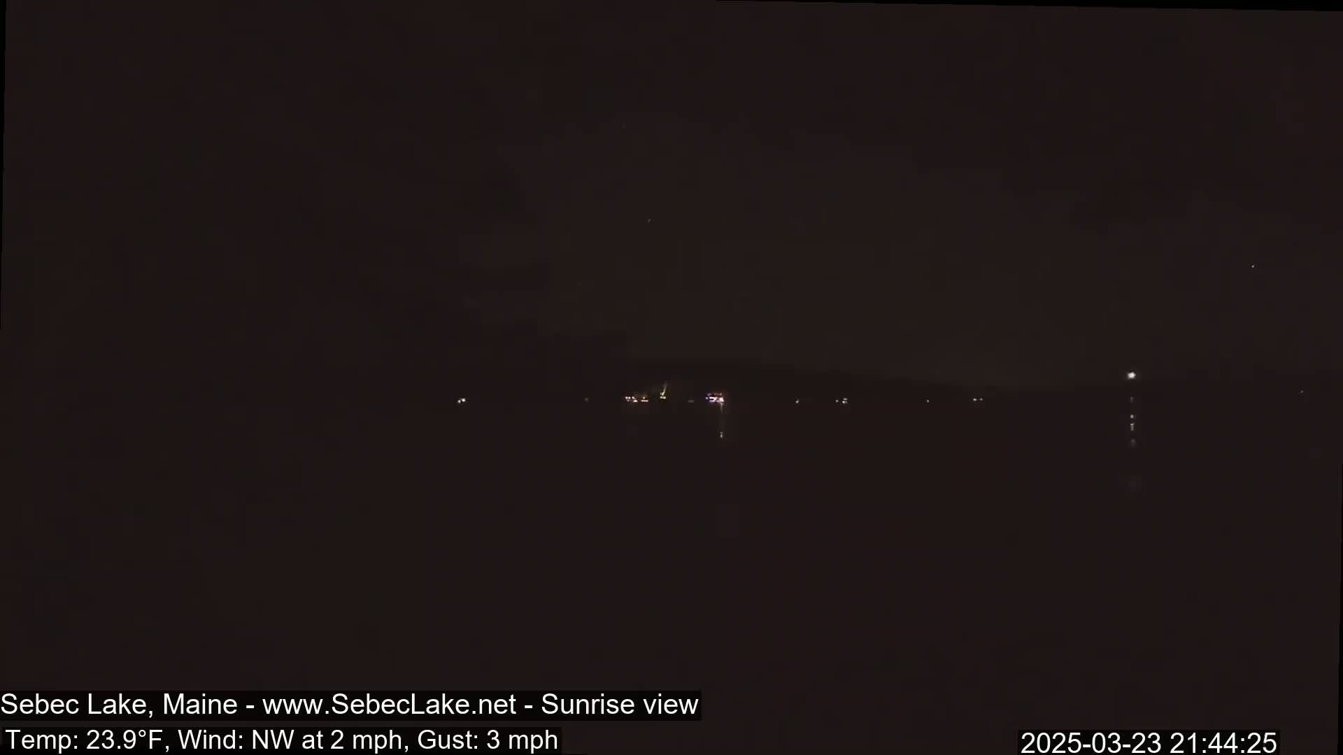 A nighttime long shot shows a dark body of water with faint lights on the far shore under a clear, dark sky.