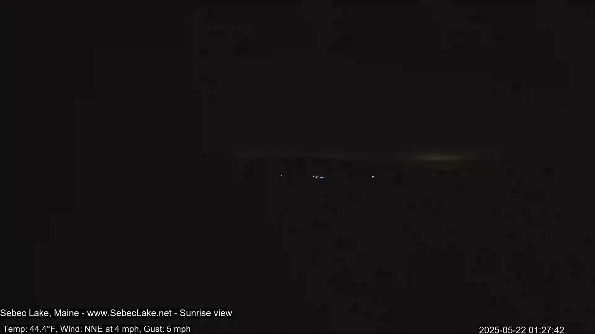 A dark, nighttime scene shows a distant horizon line with a few faint lights, under a dark sky with a NNE wind at 4 mph and gusts up to 5 mph.