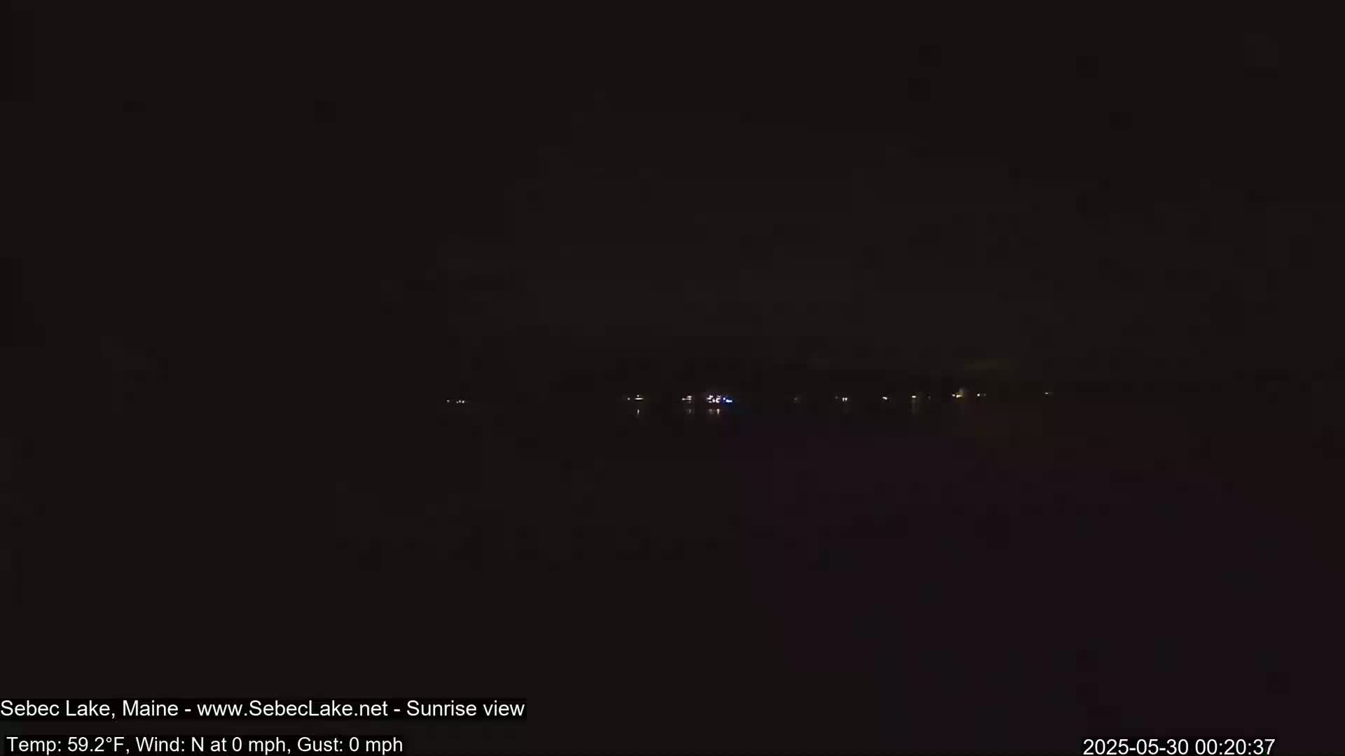 A dark nighttime view of a calm body of water with a few distant lights visible on the far shore.