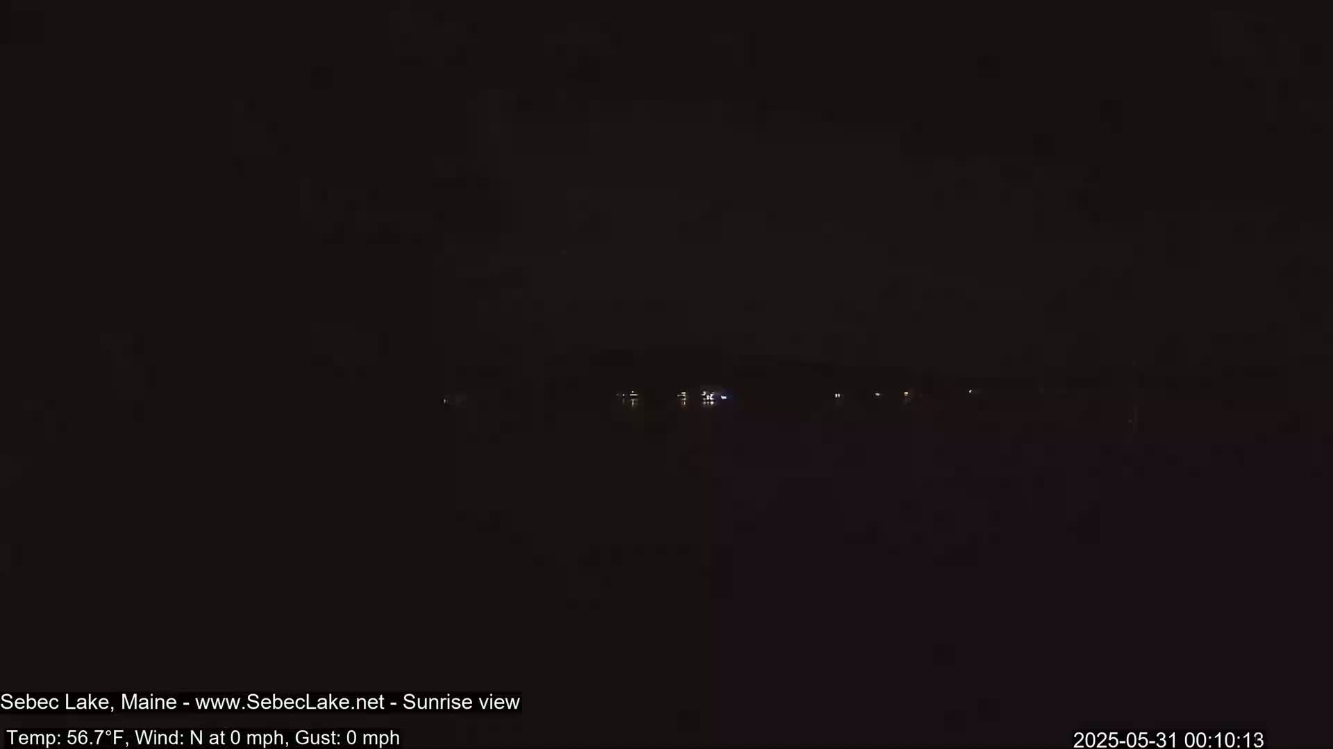A dark, nighttime view of a calm body of water with a few faint lights visible on the far shore.