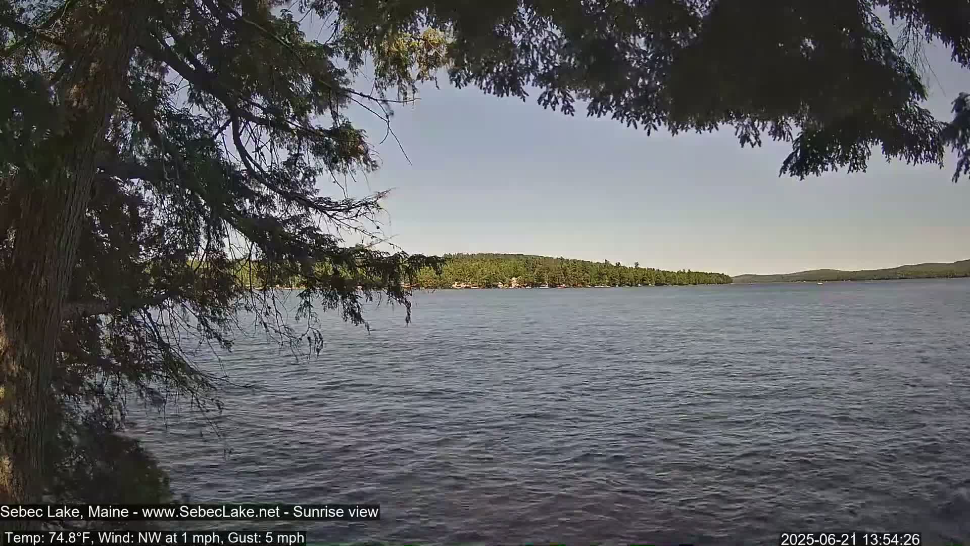 A calm lake is seen through the branches of a pine tree on a partly sunny day with a light northwest wind.
