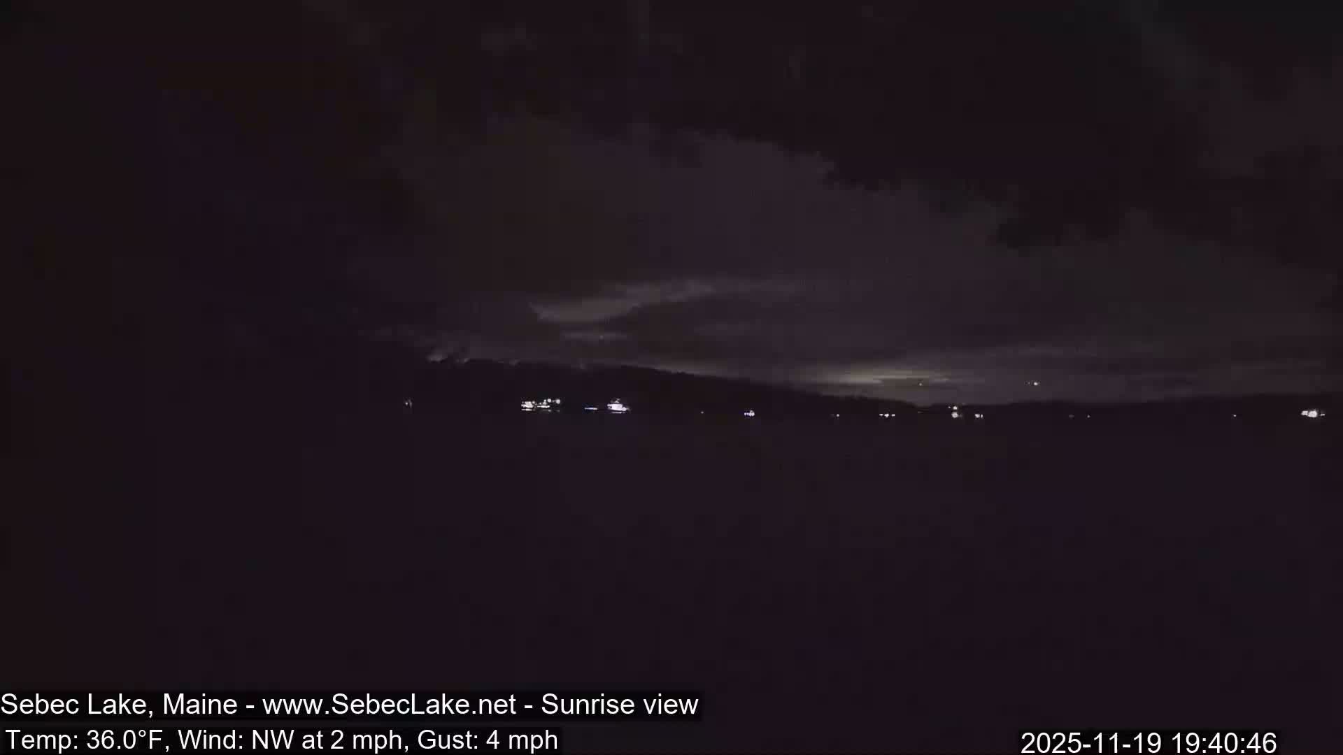 An extremely dark, pre-dawn or nighttime outdoor scene depicts a few tiny, distant lights against a backdrop of what appears to be an overcast sky.