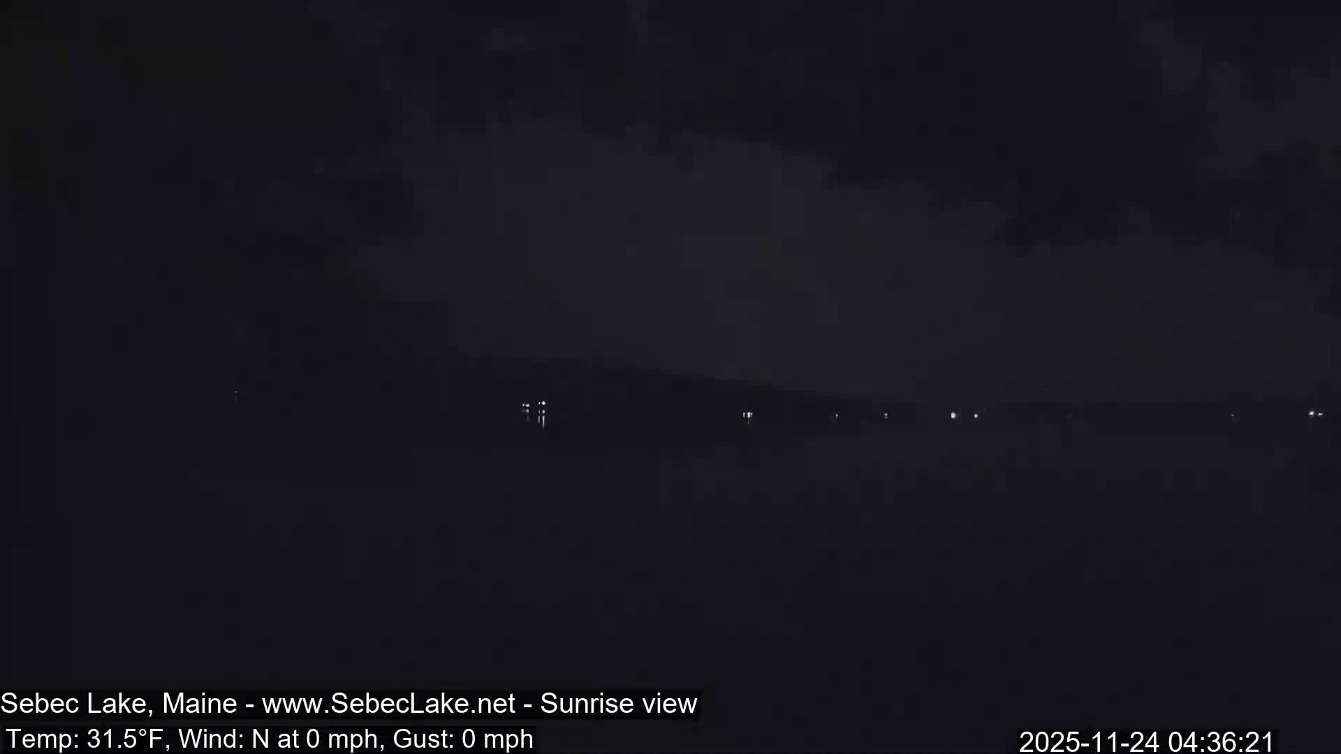 The image depicts a dark nighttime or pre-dawn scene over a body of water, with faint distant lights visible under a cloudy sky.