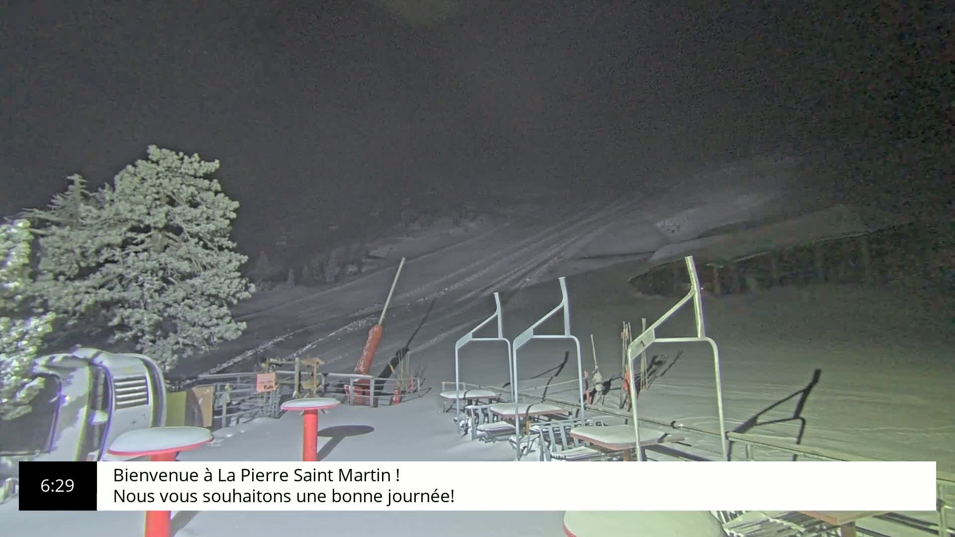 A snow-covered ski slope at night, with a chairlift and some outdoor furniture visible.