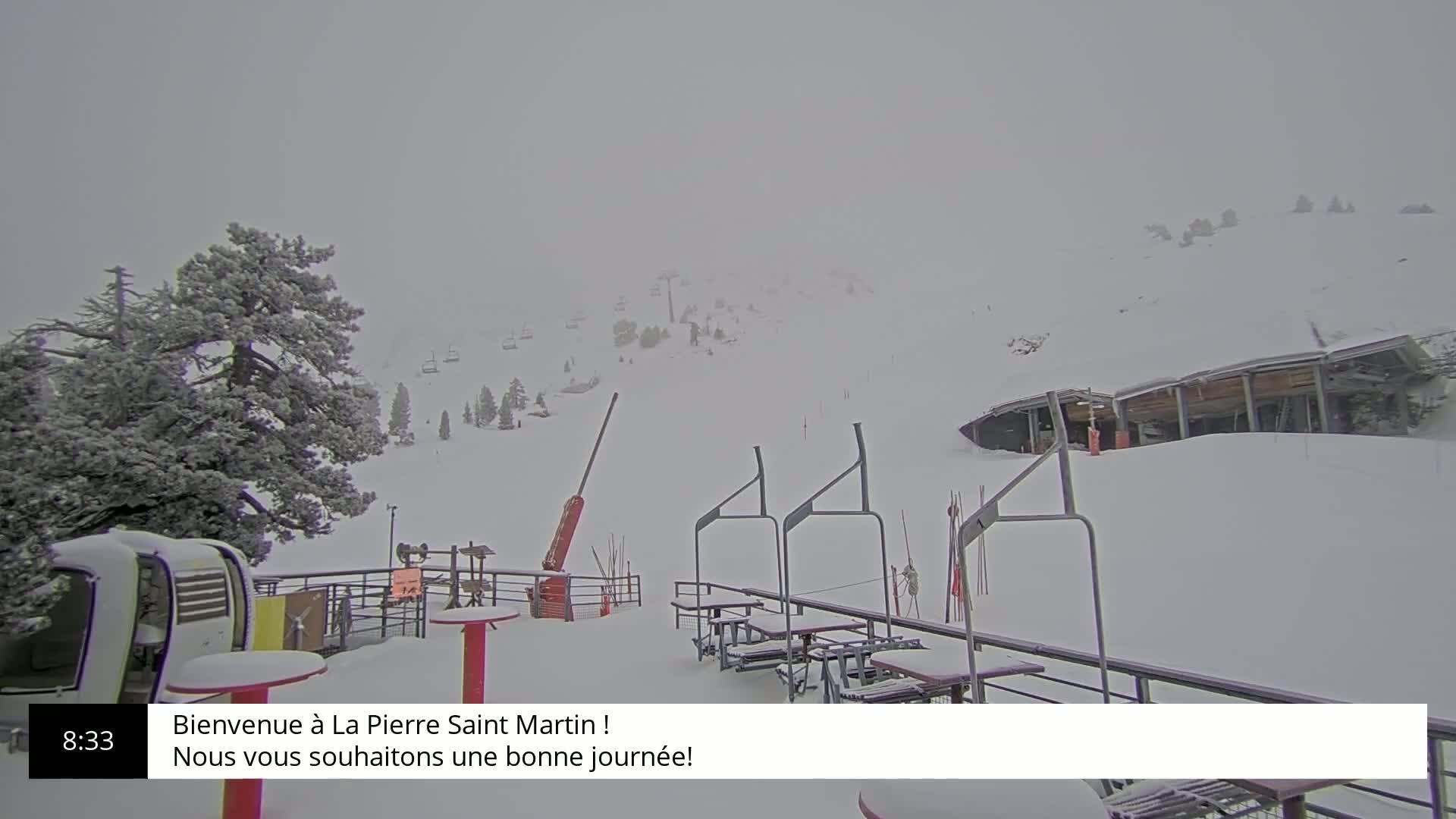 A snow-covered ski resort with chairlifts and a building partially obscured by heavy snowfall.