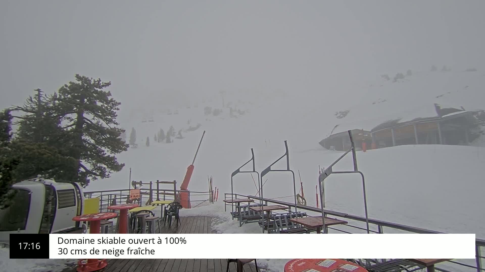 A snow-covered ski resort is visible through heavy fog, with outdoor seating and a chairlift visible in the foreground.