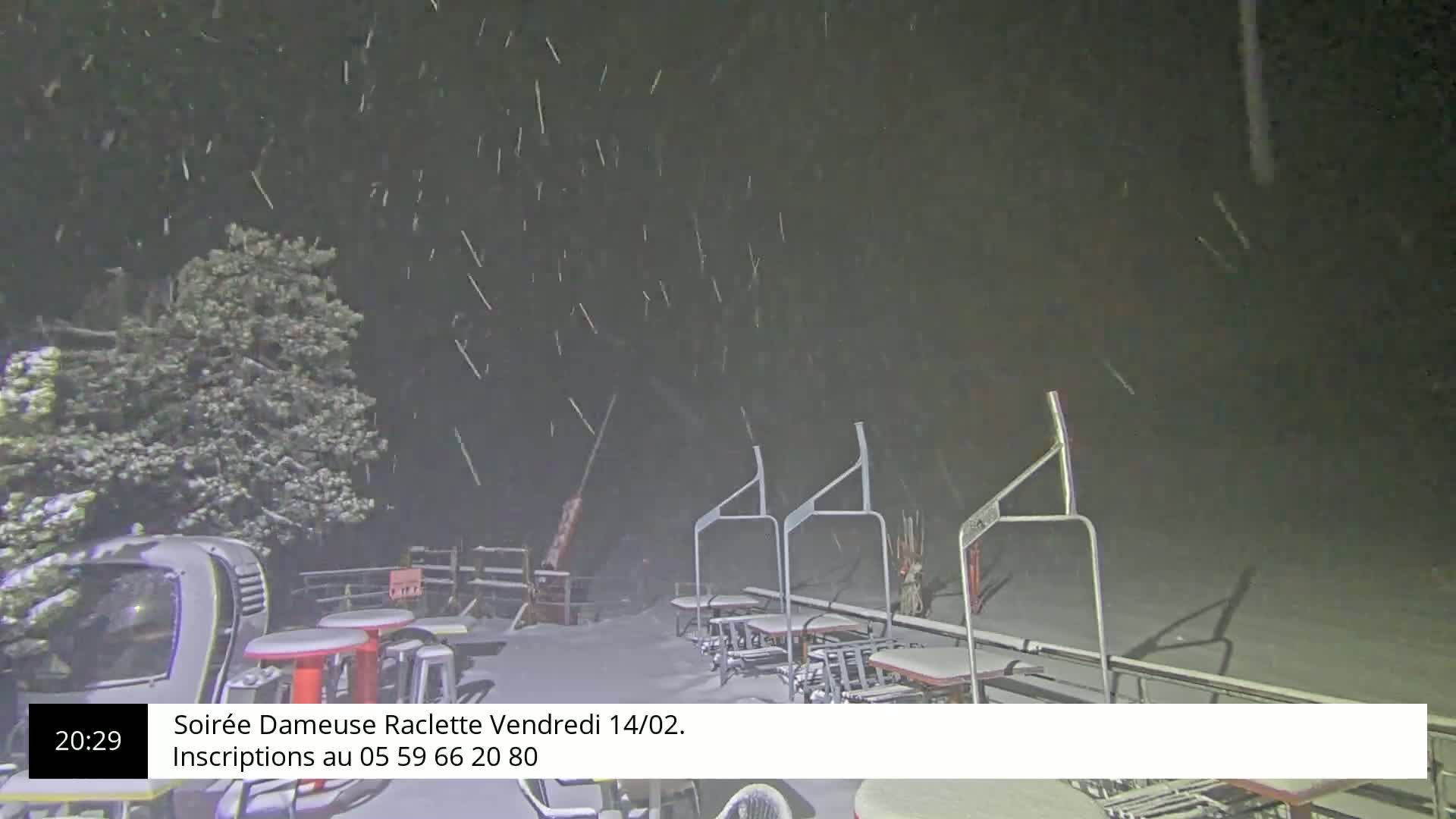 A snow-covered outdoor area with tables, chairs, and a ski lift under heavy snowfall at night.