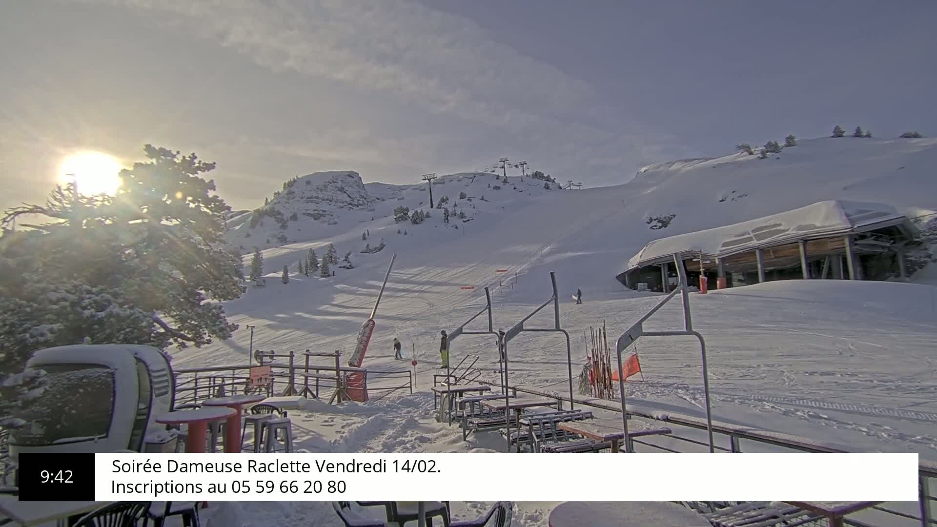 A sunny, snowy mountain slope with a ski lift and outdoor seating area.