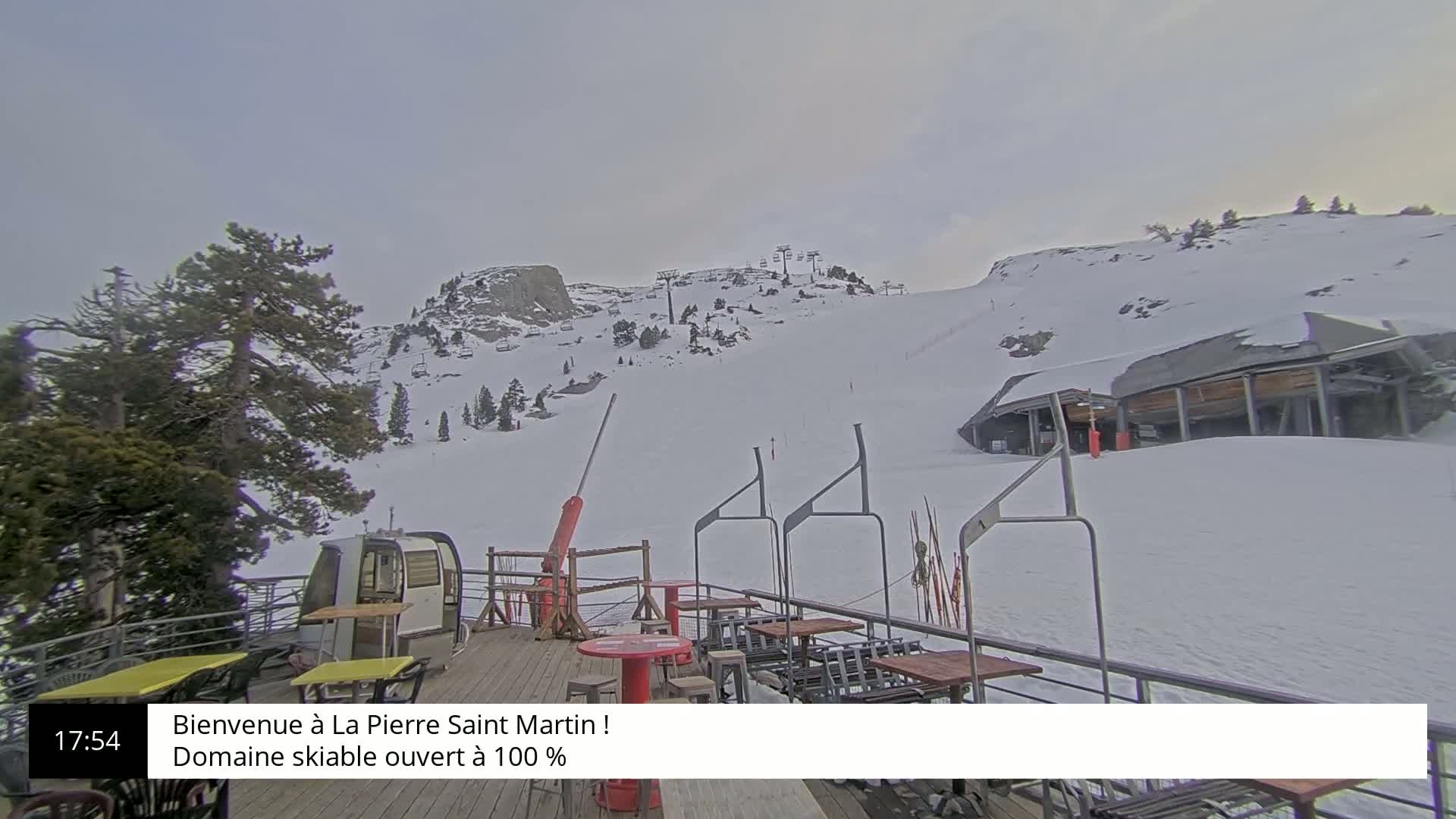 A snow-covered ski slope with lift chairs and a deck with outdoor seating is visible under an overcast sky.