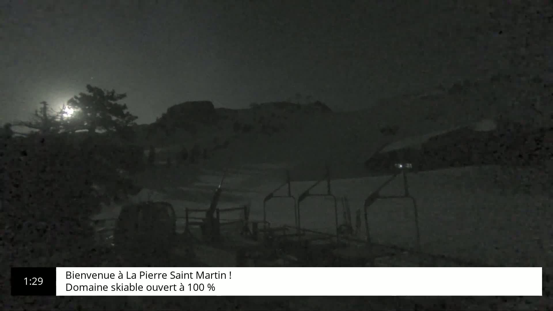 A nighttime, snow-covered ski slope is visible, with a chairlift in the foreground and a moonlit hill in the background.