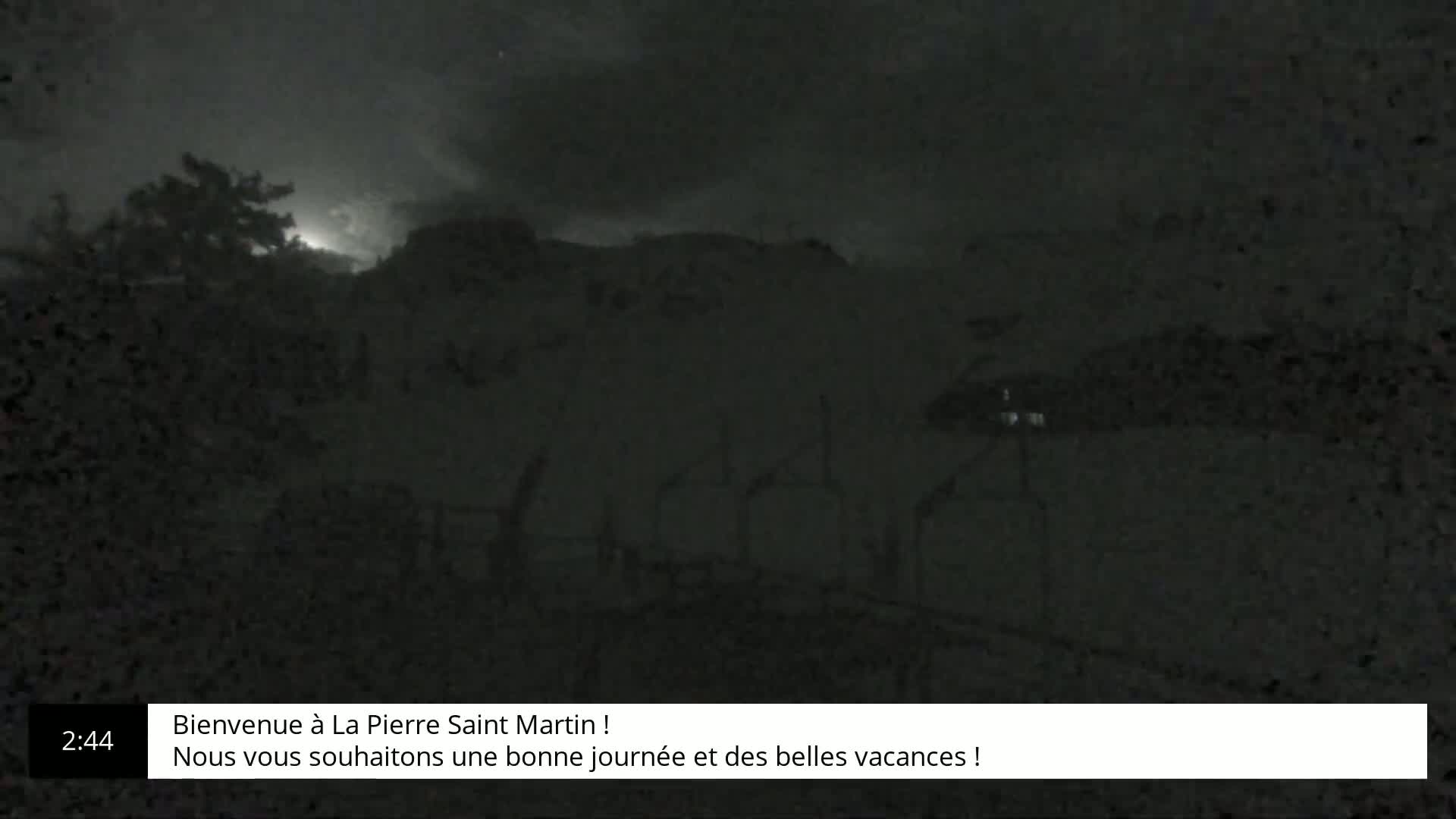 A dark, nighttime outdoor scene shows silhouetted trees and a hill under a cloudy sky with a possible lightning strike in the distance.