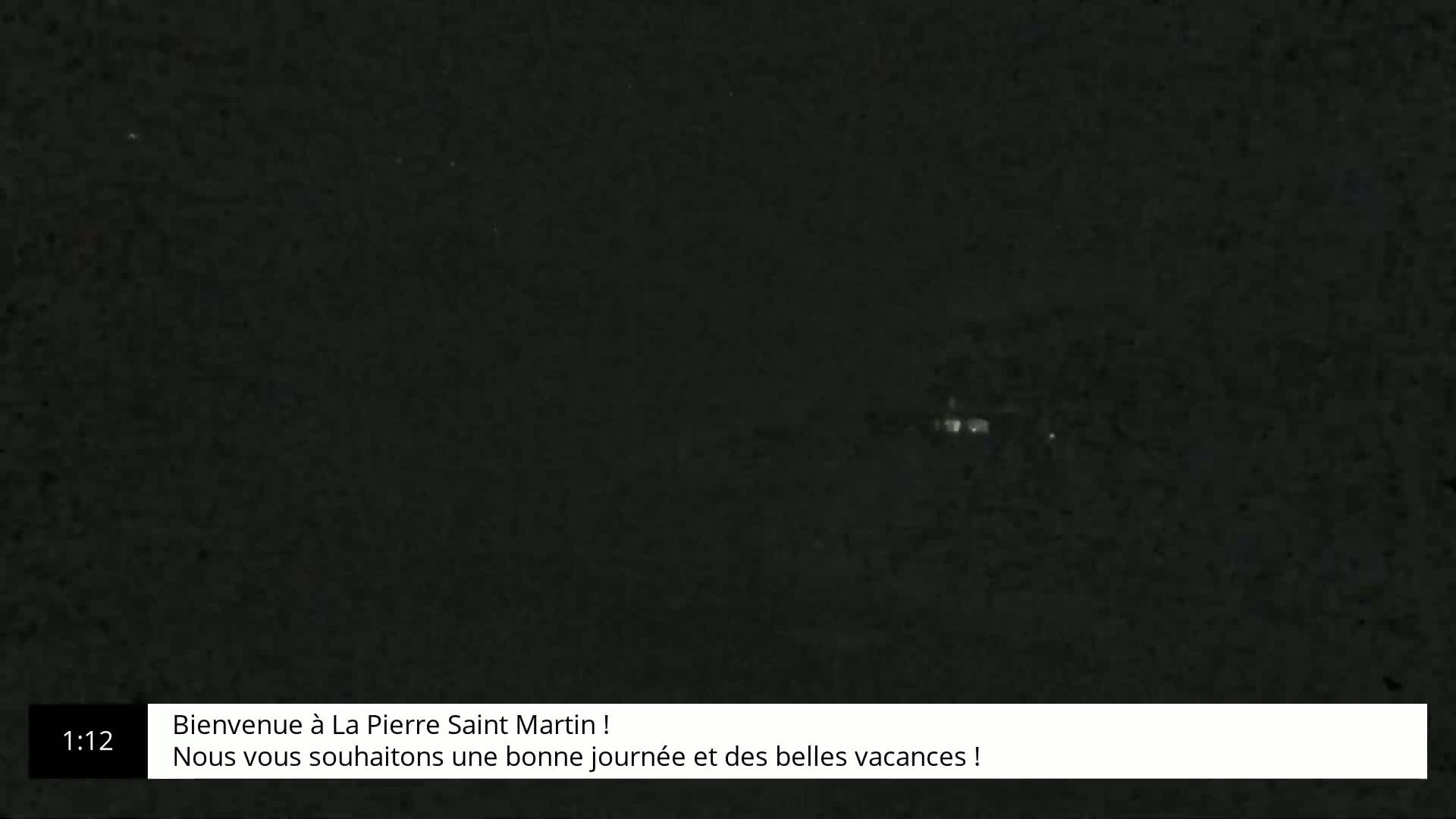 A nighttime, low-light view of a dark landscape with a few faintly visible lights in the distance.