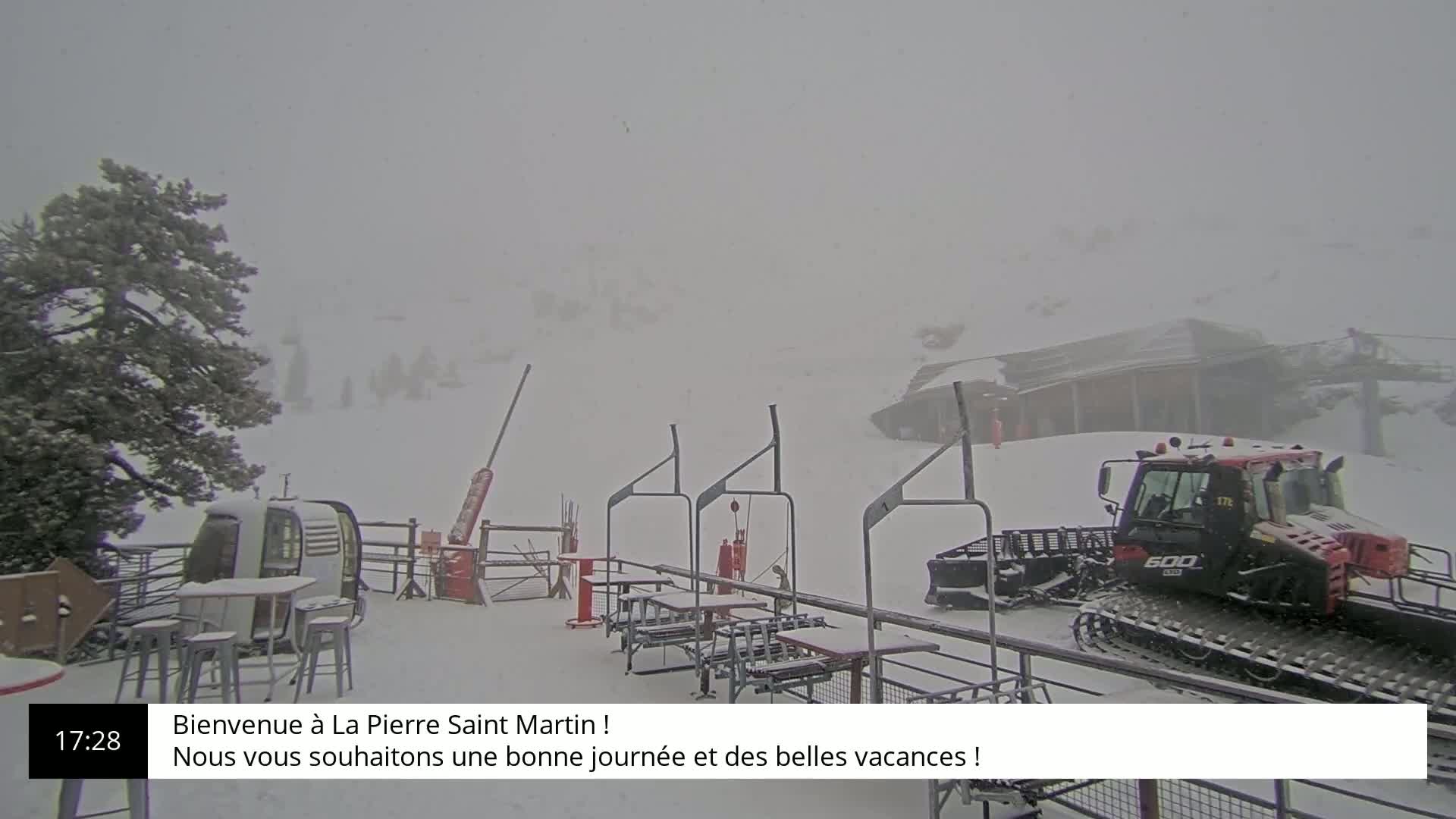A snowcat is parked near a snow-covered ski lift during a heavy snowstorm.