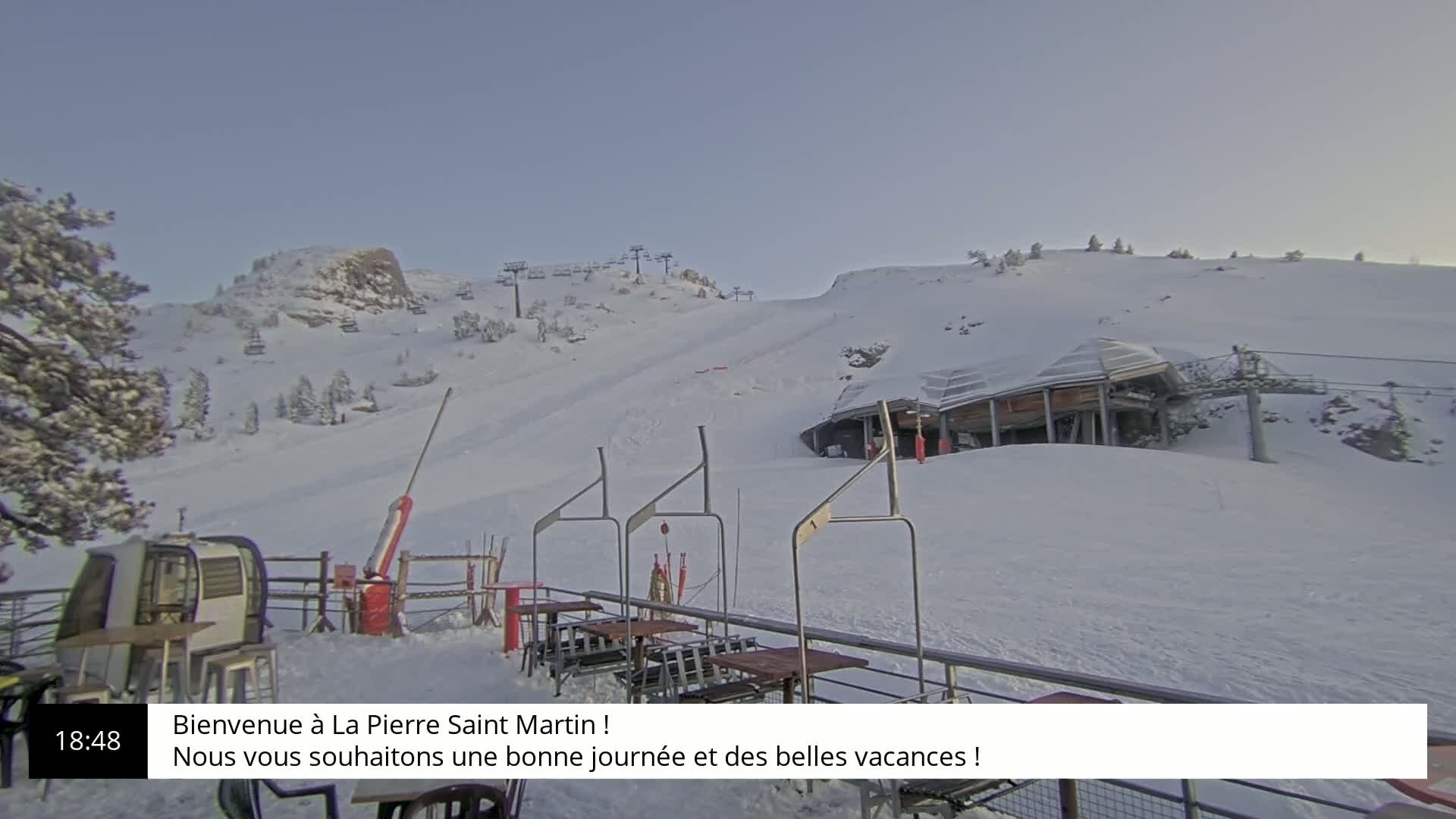 A snow-covered ski resort with a lift and a building in the background under a clear sky.