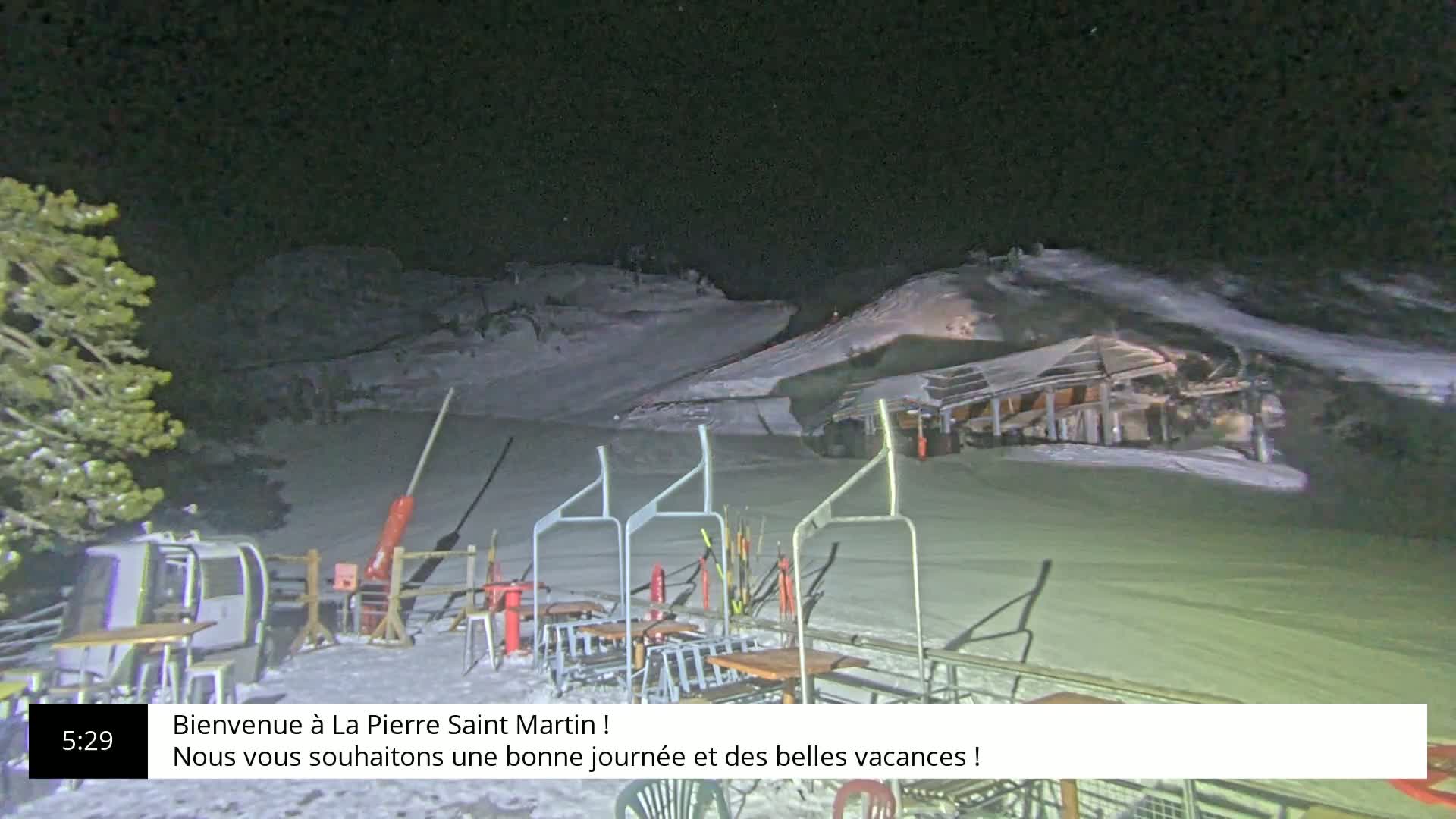 A nighttime view of a snow-covered ski resort with a chairlift and several tables and chairs.