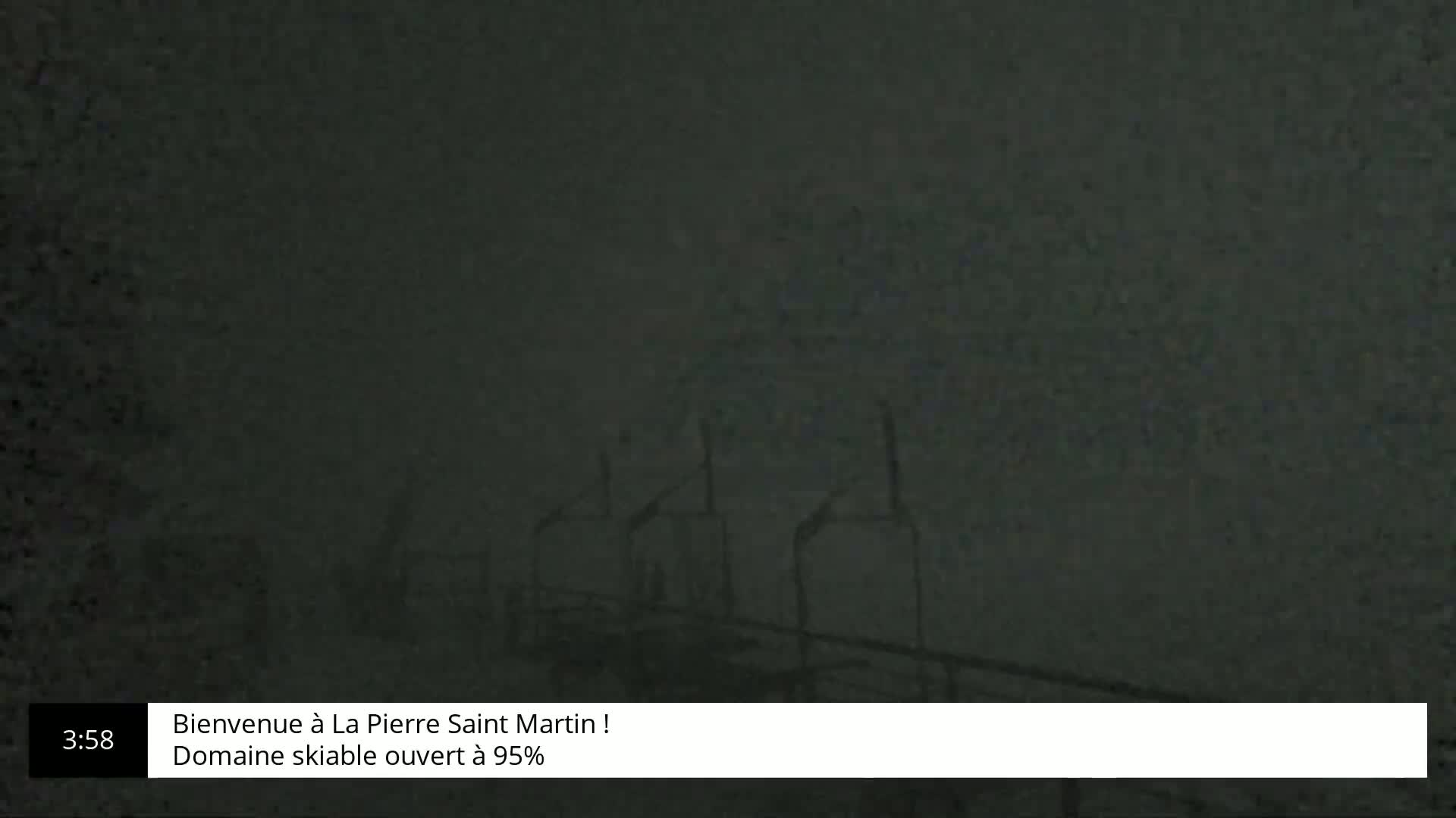 A dark, blurry image shows what appears to be several structures or buildings in foggy or snowy conditions at night.
