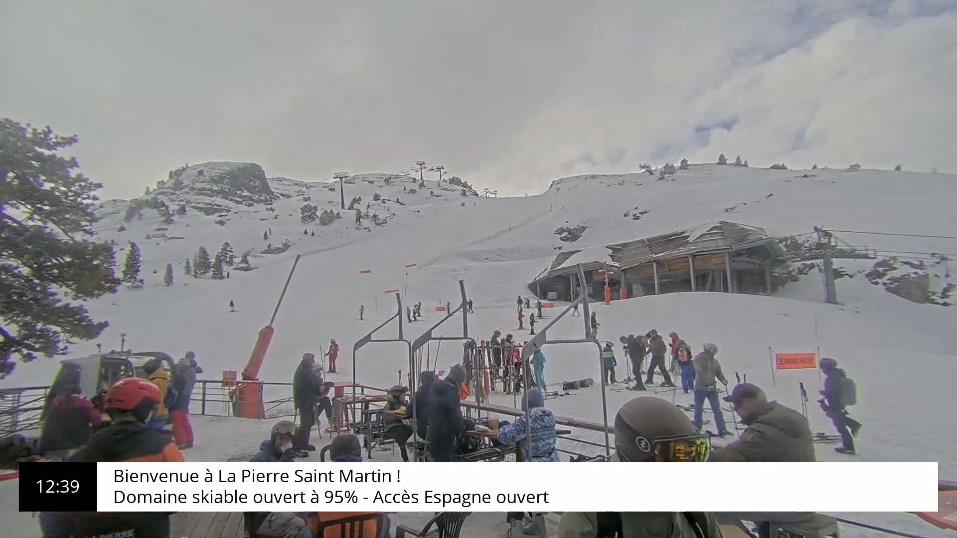 A snowy ski slope with several skiers and snowboarders near a lift station under an overcast sky.