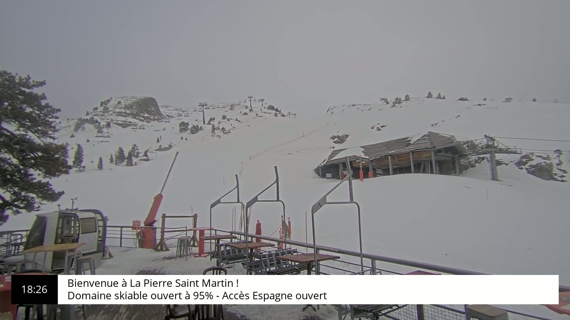 A snowy ski resort on an overcast day, showing a chairlift and a building on a snow-covered hillside.