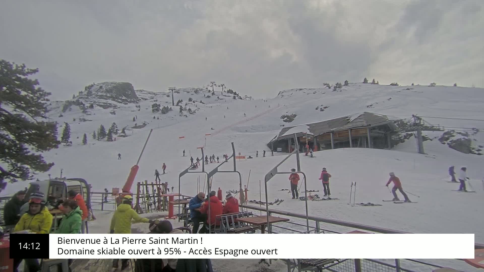 A snowy ski slope with several skiers and a lift station under an overcast sky.